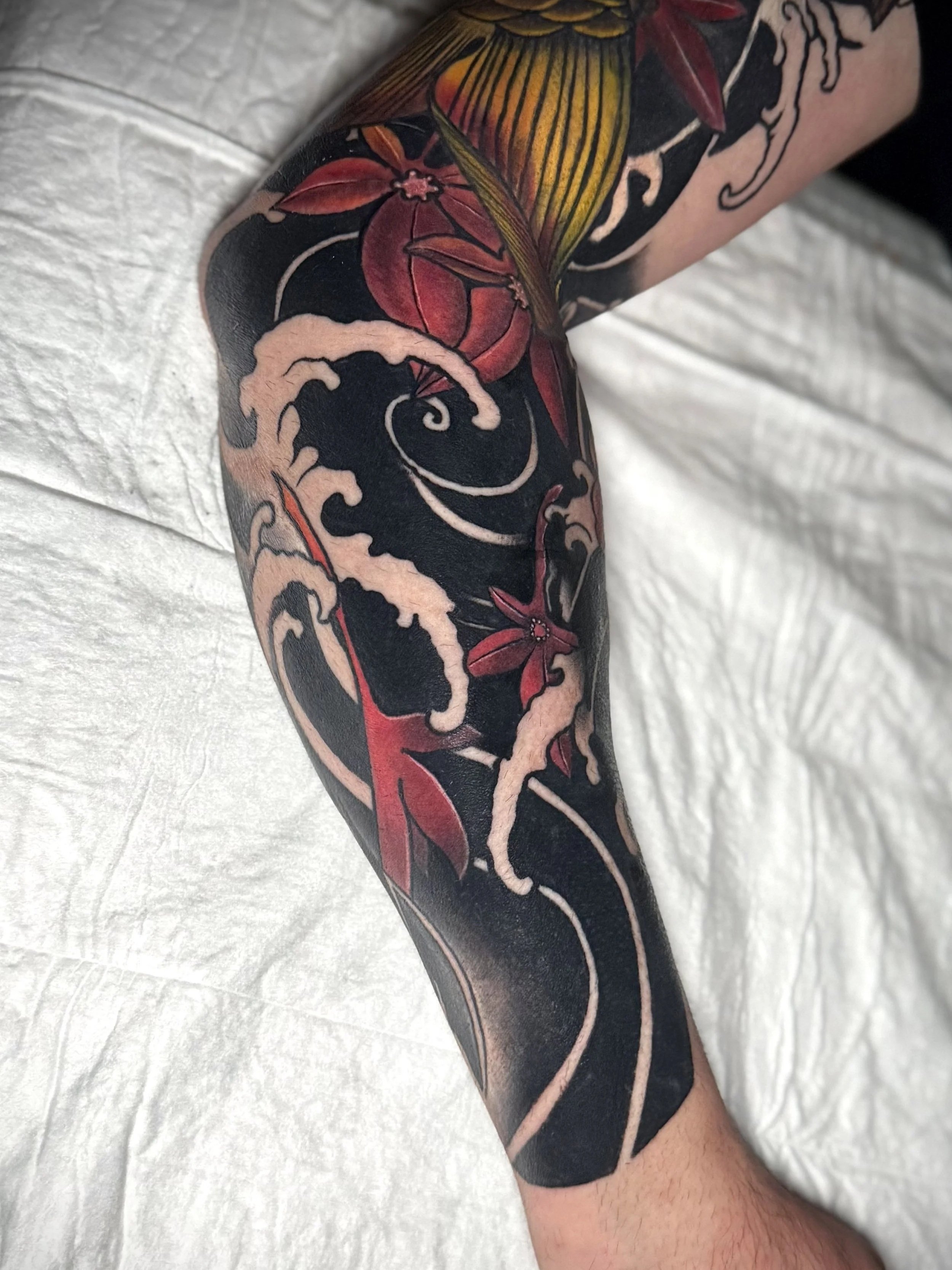 Tattoo auf einem Arm, das eine Welle und Blumen in japanischer Stil zeigt.
