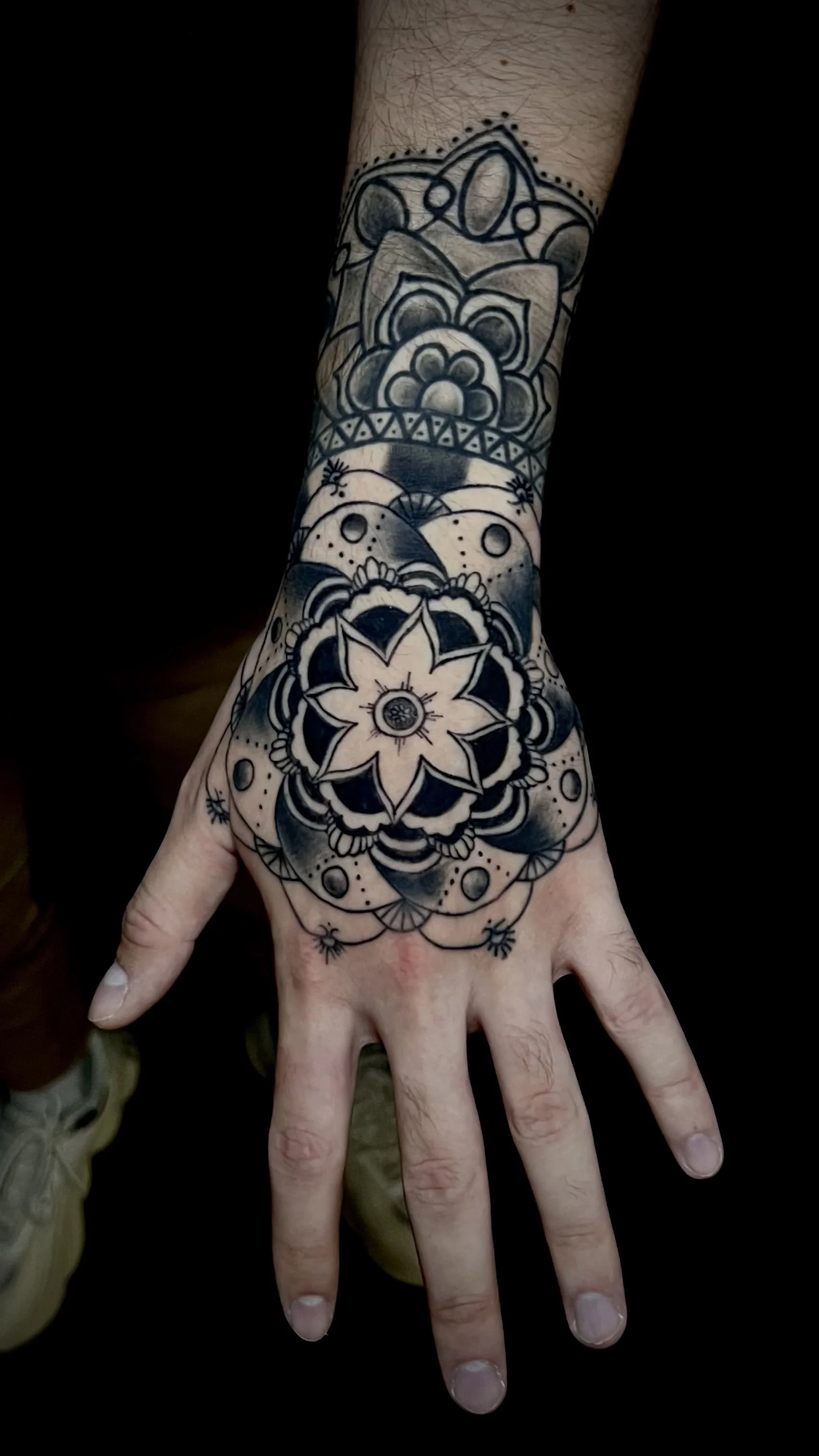 Schwarze Tätowierung auf der Hand und dem Handgelenk mit Blumen- und geometrischen Mustern.