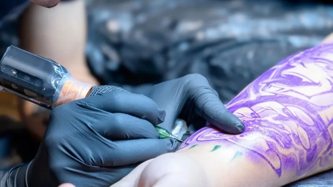Tattoo-Künstler beim Einsetzen eines Tattoo-Siegels auf einem Arm, während der Arm bereits mit einem Schutzfilm bedeckt ist.