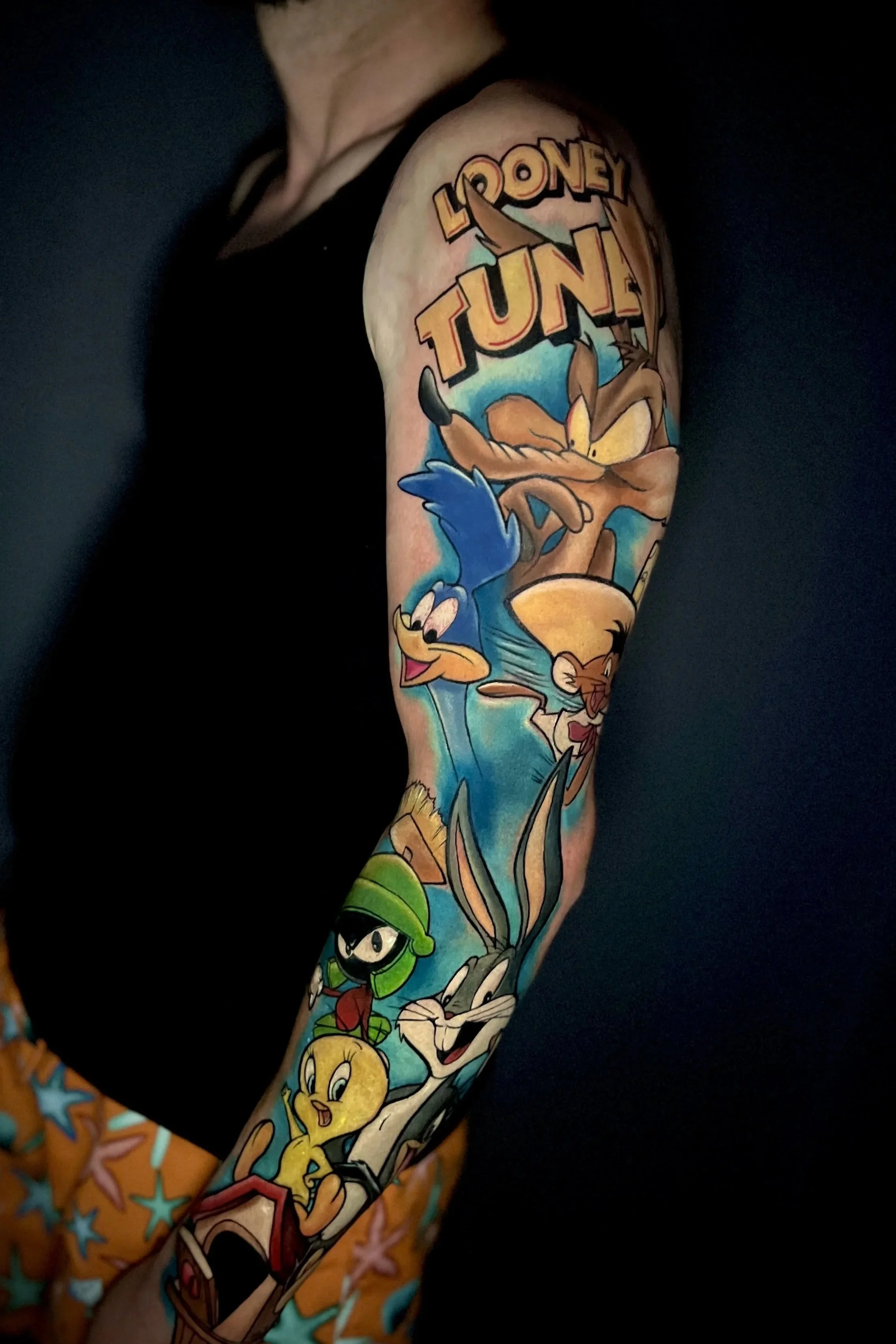 Tattoo mit Looney Tunes Charakteren auf dem Arm, inklusive Taschenmonster, gelbe Ente, Ninjakämpfer und andere Figuren in farbenfrohem Stil.