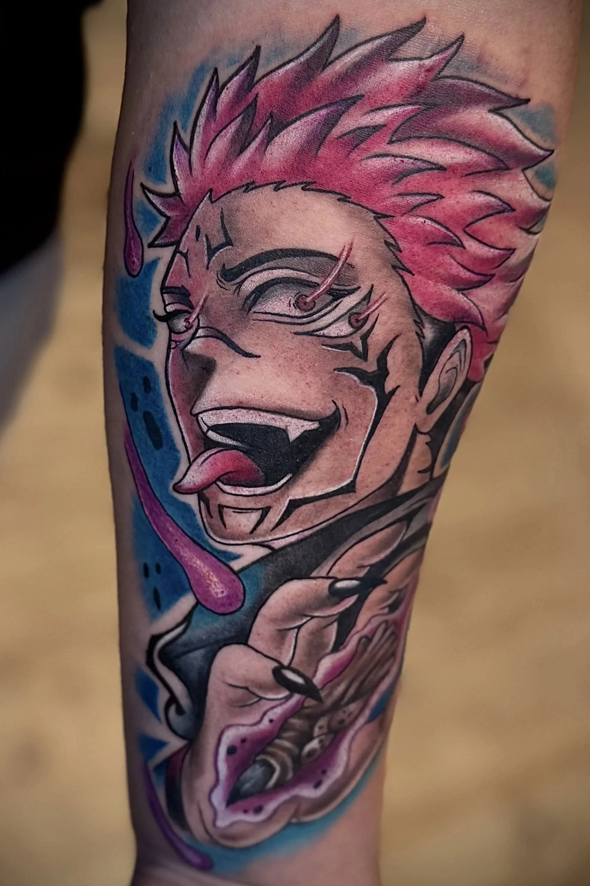 Ein buntes Tattoo auf einem Arm, das einen lachenden, comicartigen Charakter mit pinken, spitzen Haaren, einer Zunge und einem breiten Lächeln zeigt.