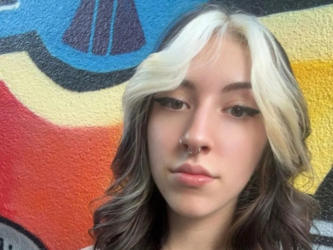 Nahaufnahme eines jungen Mädchens mit schwarzem und platinblondem Haar vor einer bunten Wand mit Graffiti