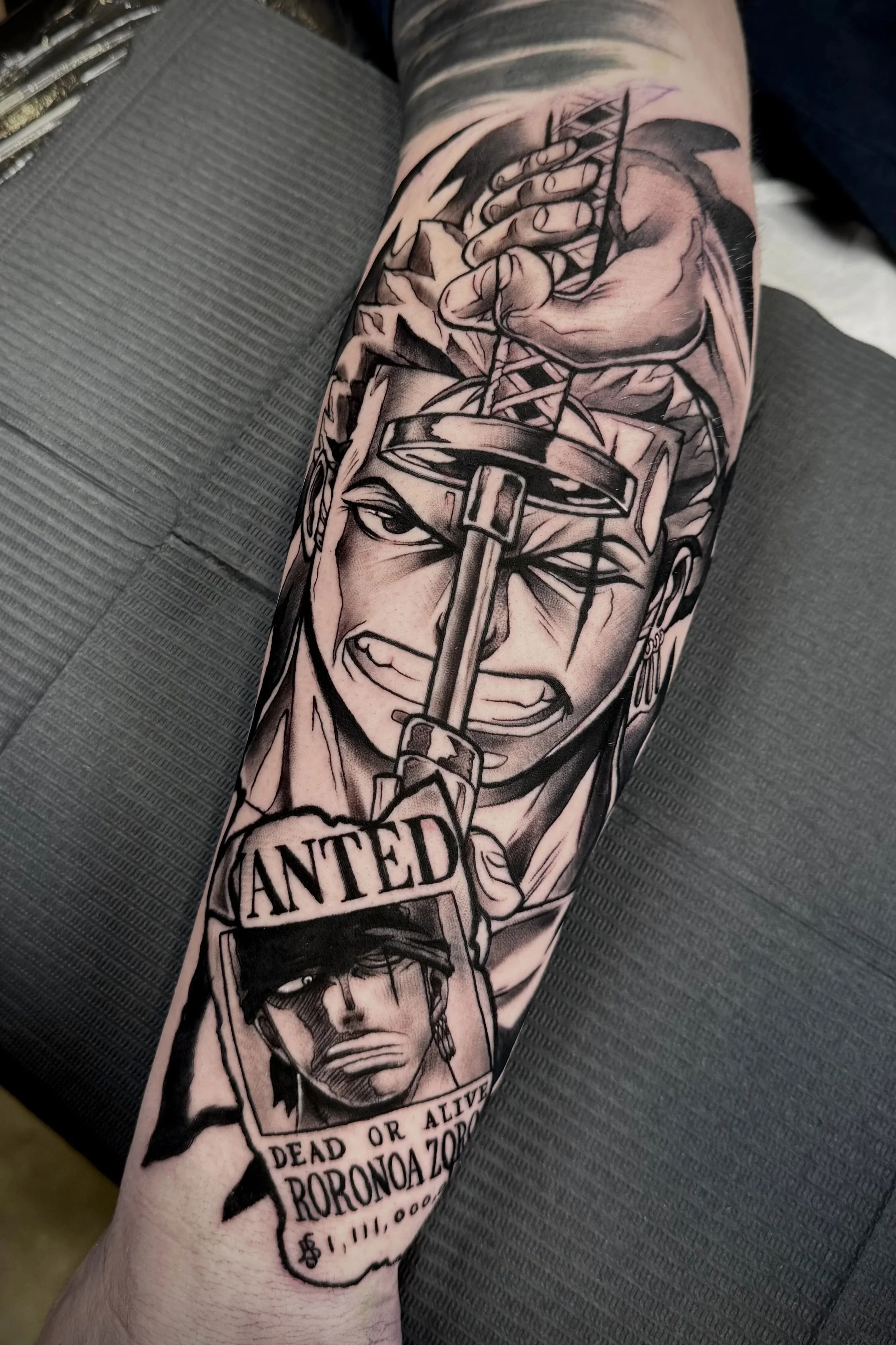 One Piece Tattoo mit Roronoa Zoro und Wanted-Poster in Black & Grey auf dem Unterarm.