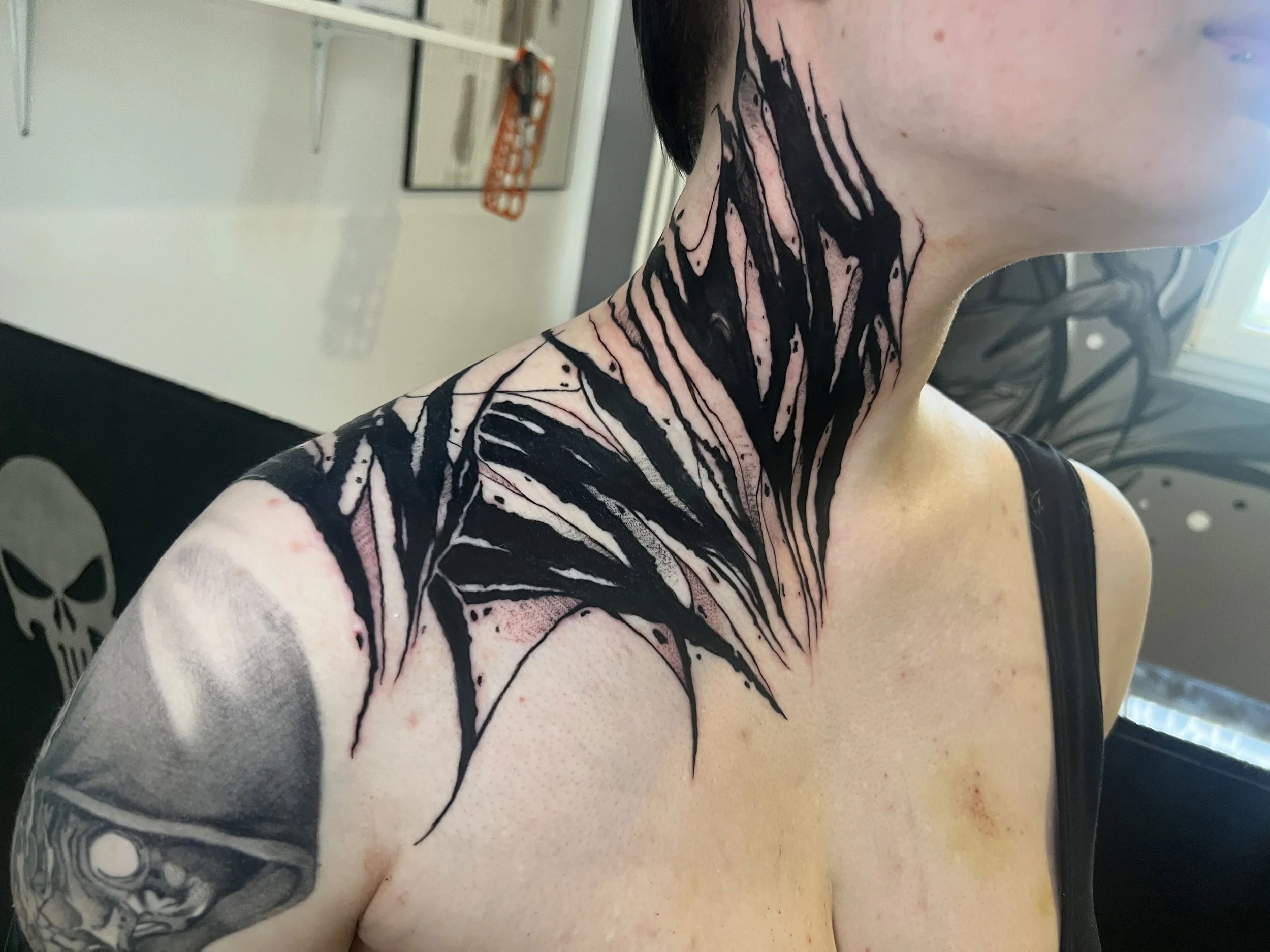 Nahaufnahme eines Schulter- und Armtattoos mit schwarzen Linien und Mustern auf heller Haut.