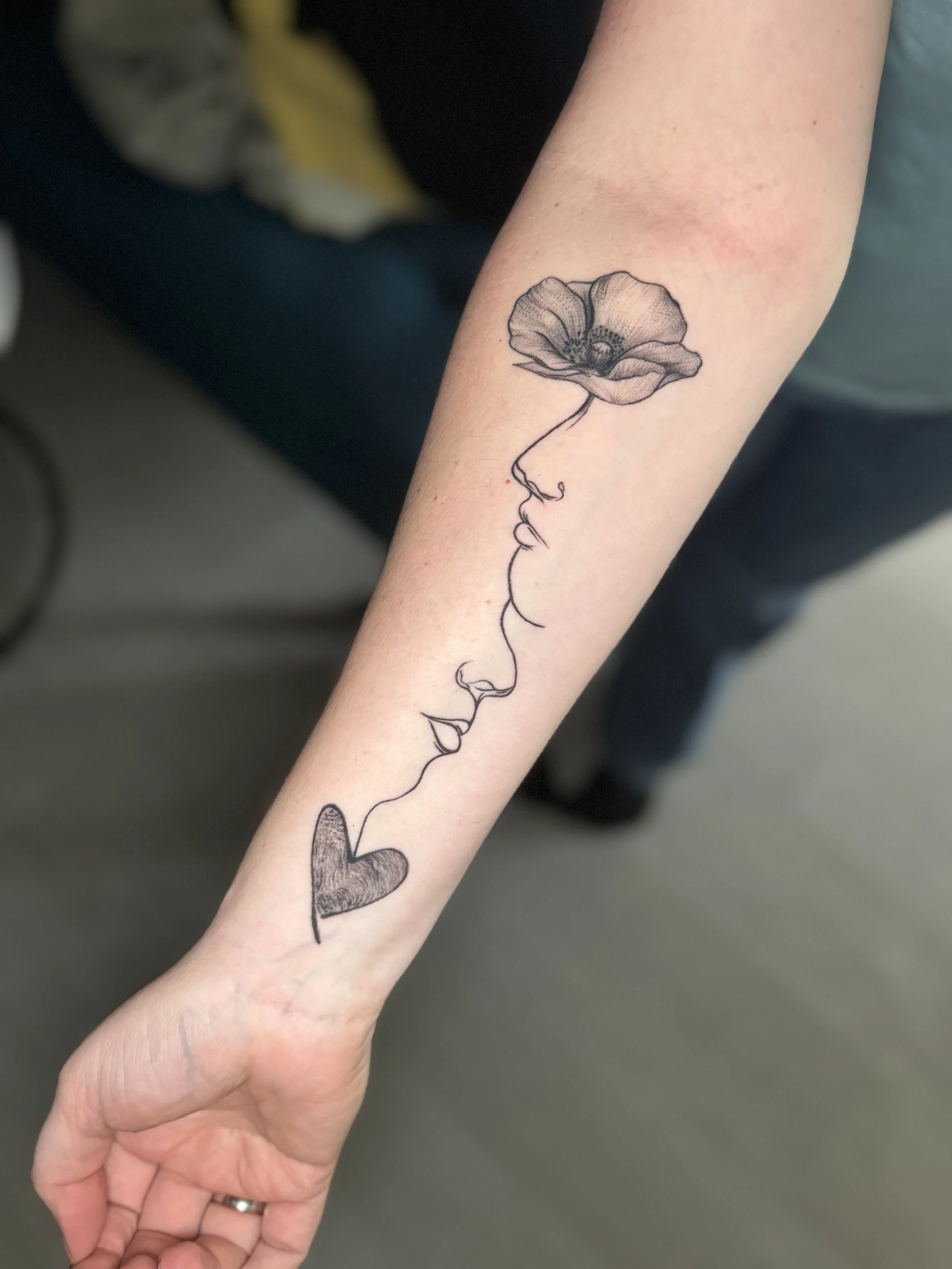 Tattoo eines Gesichts im Profil, das aus einer Blume besteht, auf dem Unterarm.