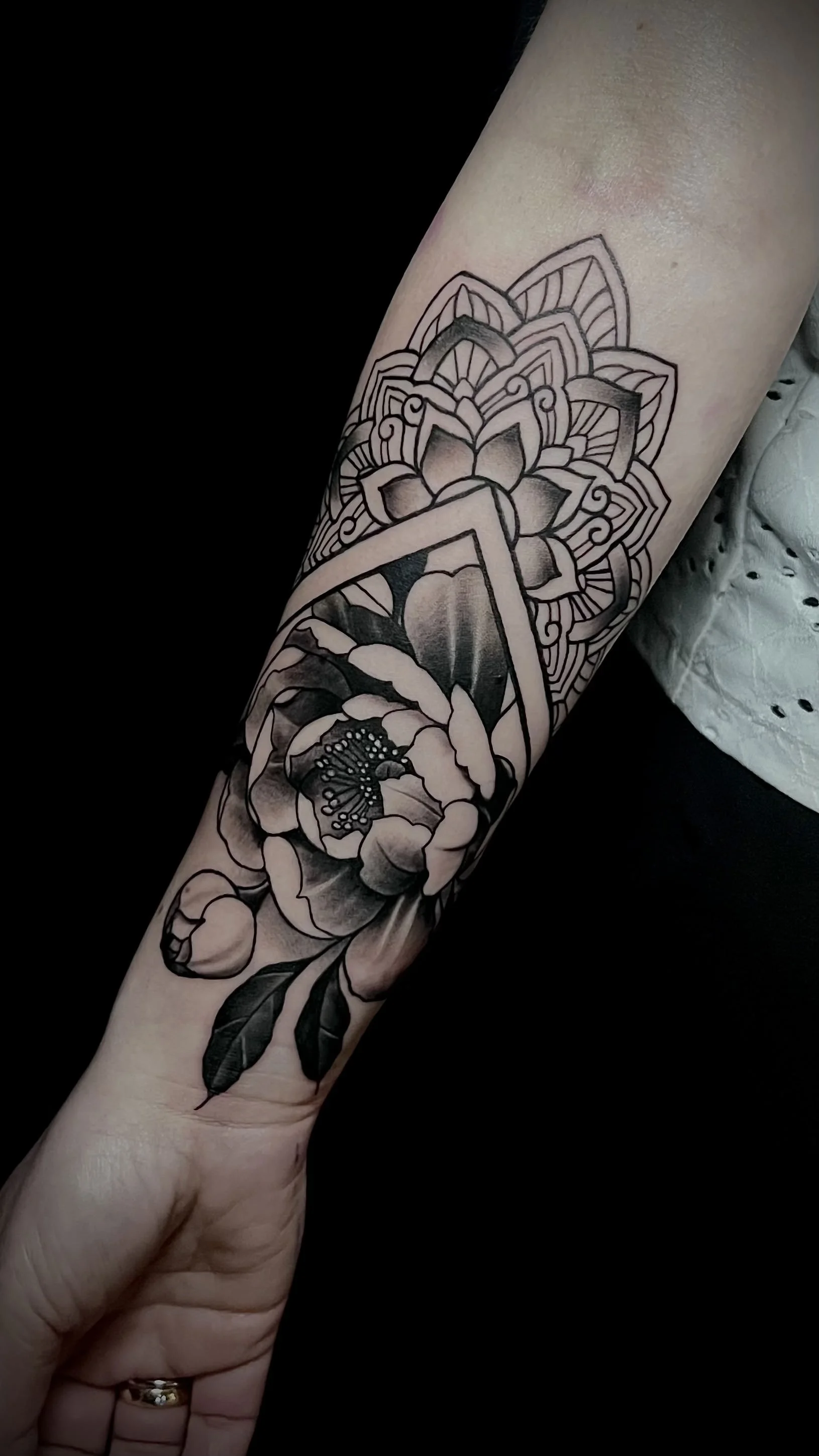 Schwarze Tätowierung eines Blumenmusters auf dem Unterarm einer Person.