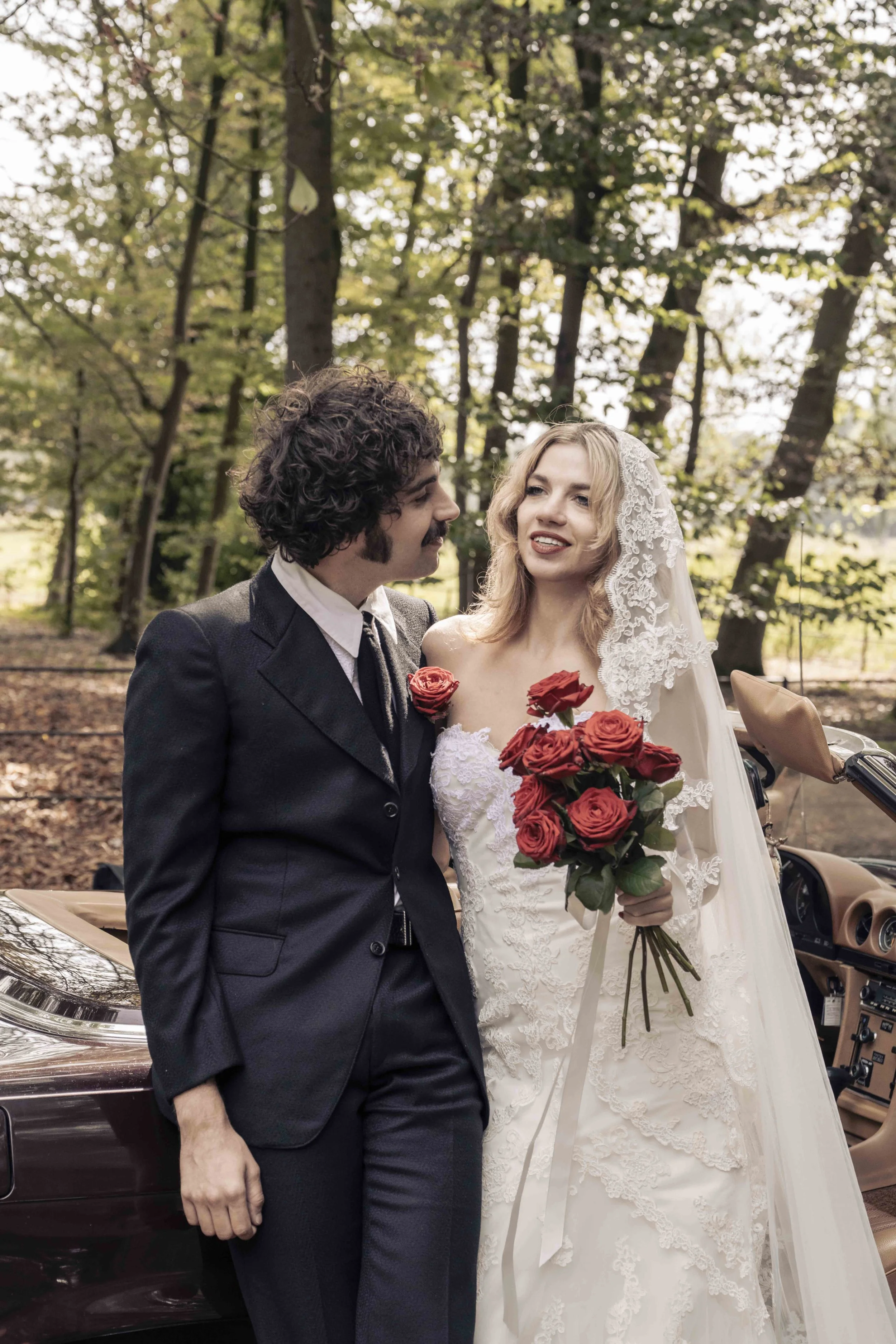 Een man en vrouw in een bos, getrouwd, de vrouw houdt een bos rozen, zij draagt een kanten bruidsjurk en een sluier.
