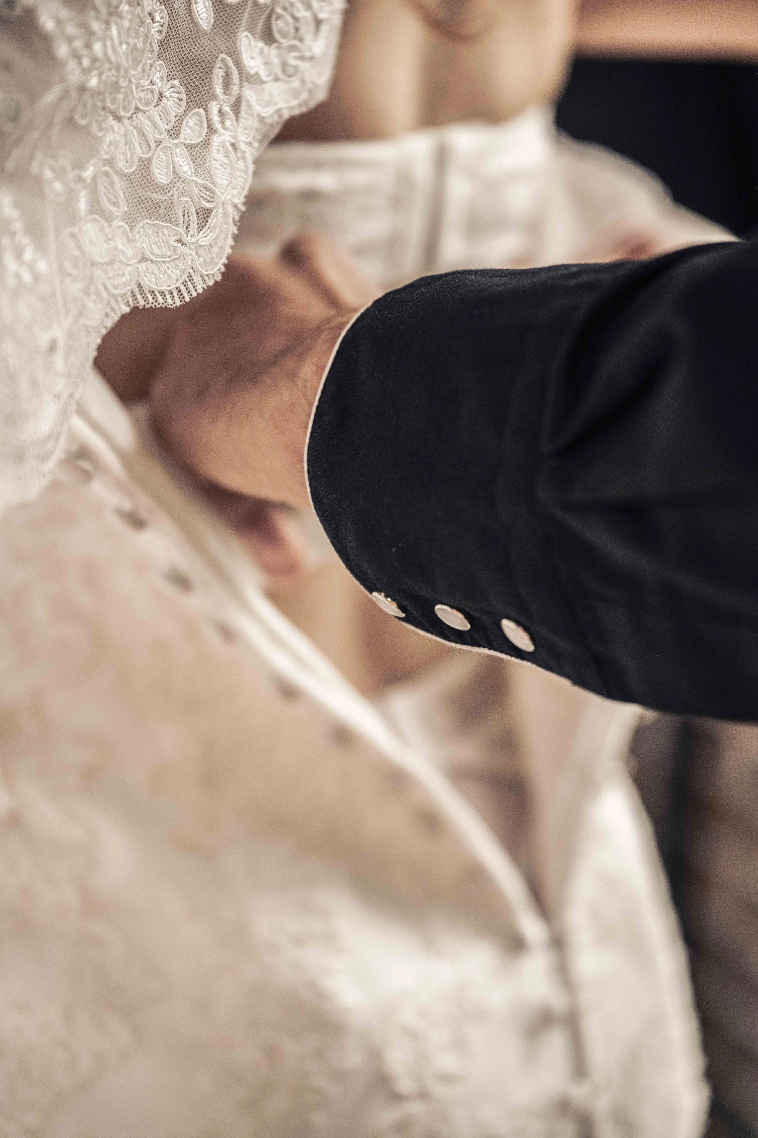 Close-up van een bruid die een jurk met kant en een vriend of familielid die een donker pak en witte manchetten draagt, tijdens een bruiloft.