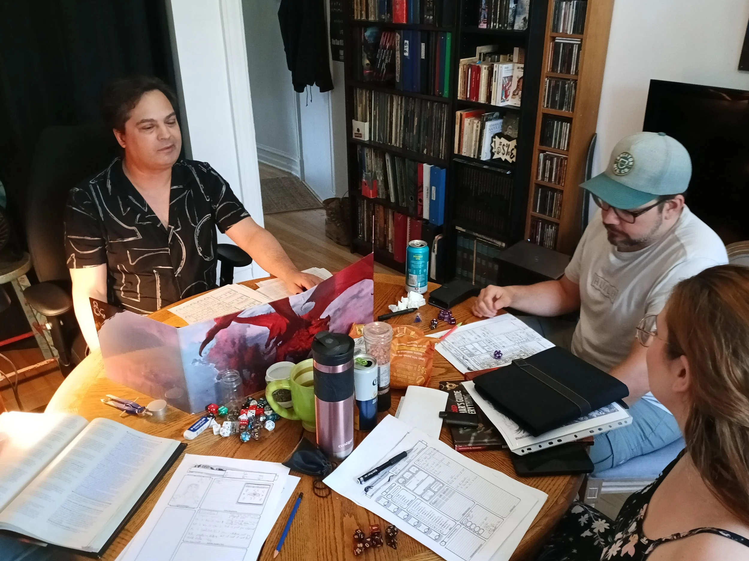 Groupe de plusieurs personnes jouant à un jeu de rôle autour d'une table avec des dés, des livres et des notes.