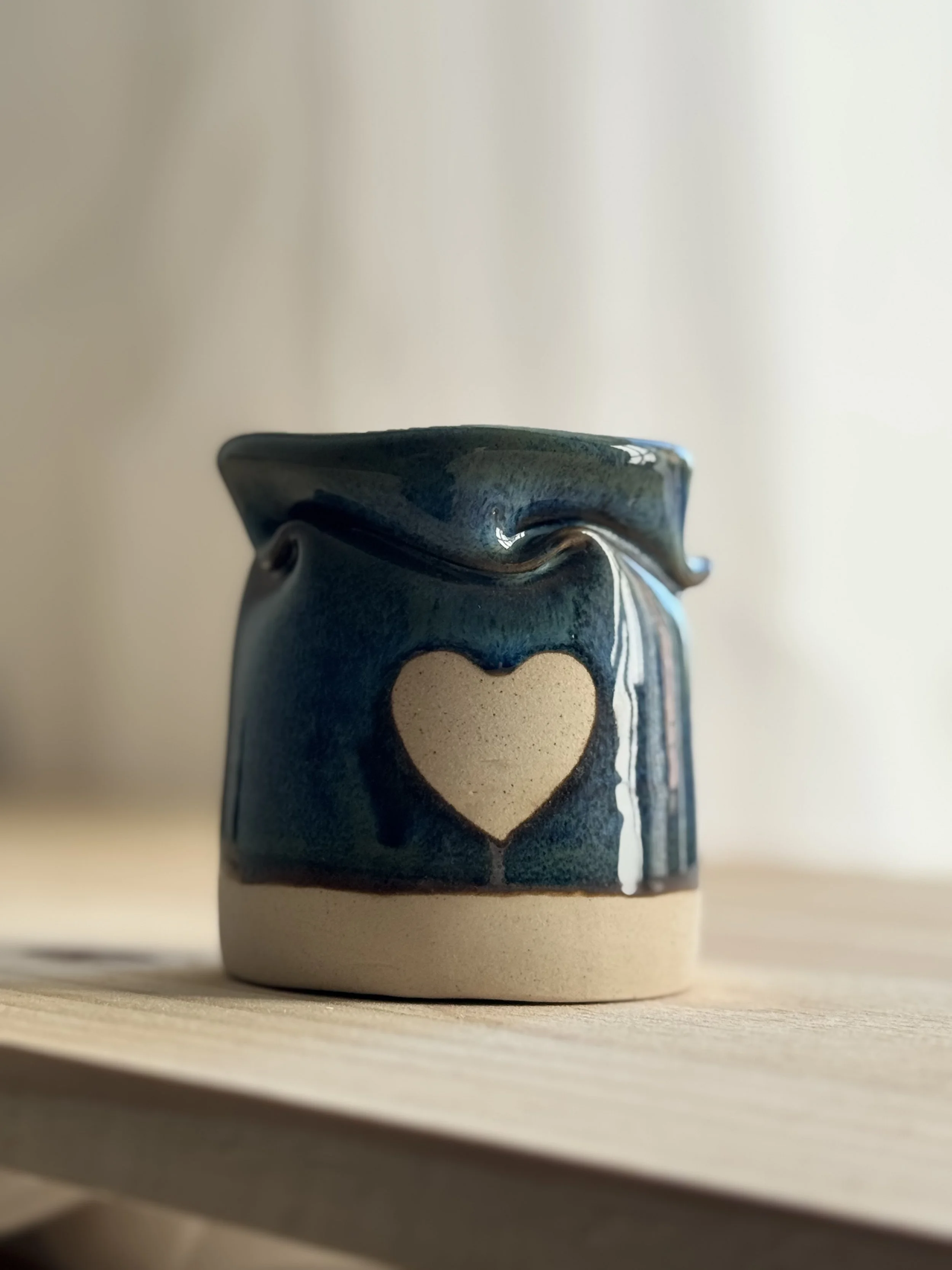 Close-up of a ceramic pot with a heart shape cut-out on a wooden surface.