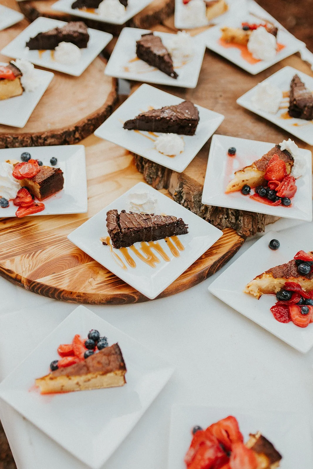 Cake slices are shown on white square plates, topped with fresh berries and caramel drizzle