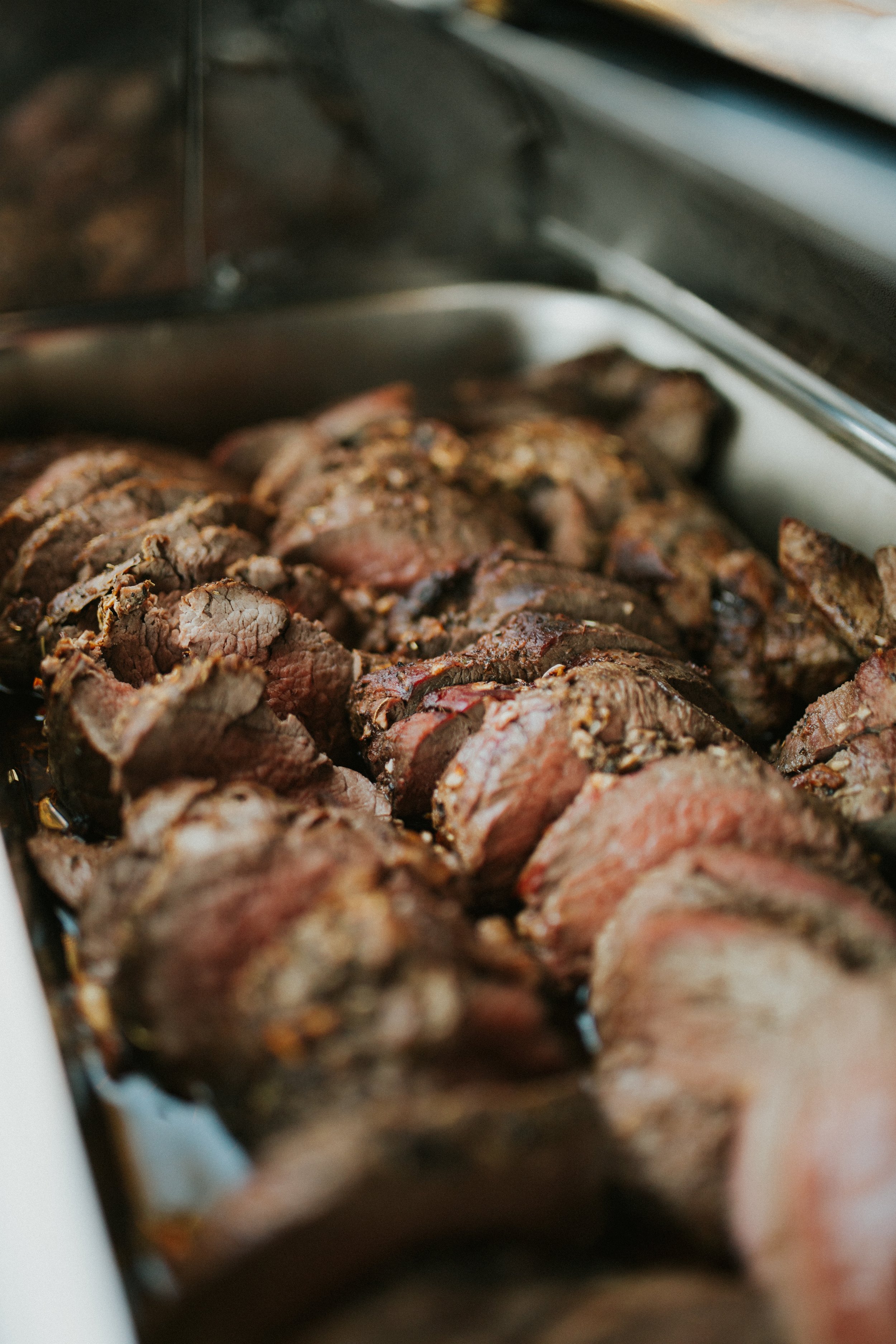 Close-up of sliced, cooked steak lined up in a silver pan.