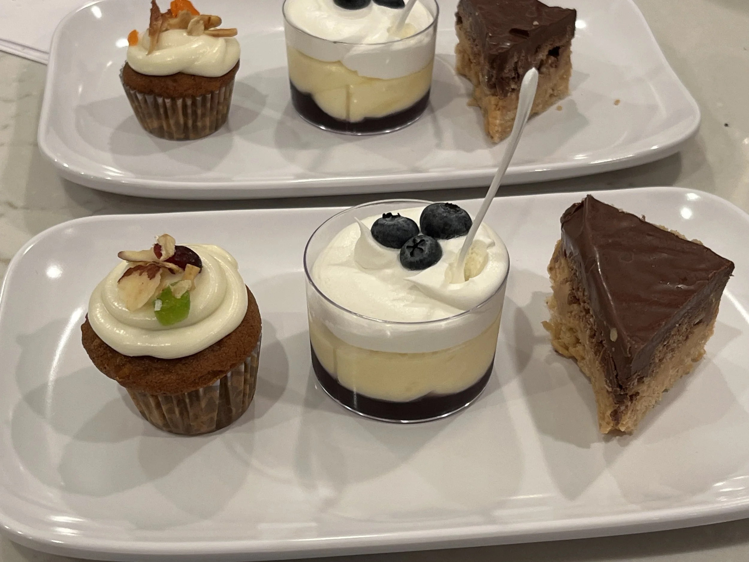 Assorted desserts on white serving trays, including mini carrot cupcakes , lemon + blueberry mousse, and chocolate peanut butter confection.