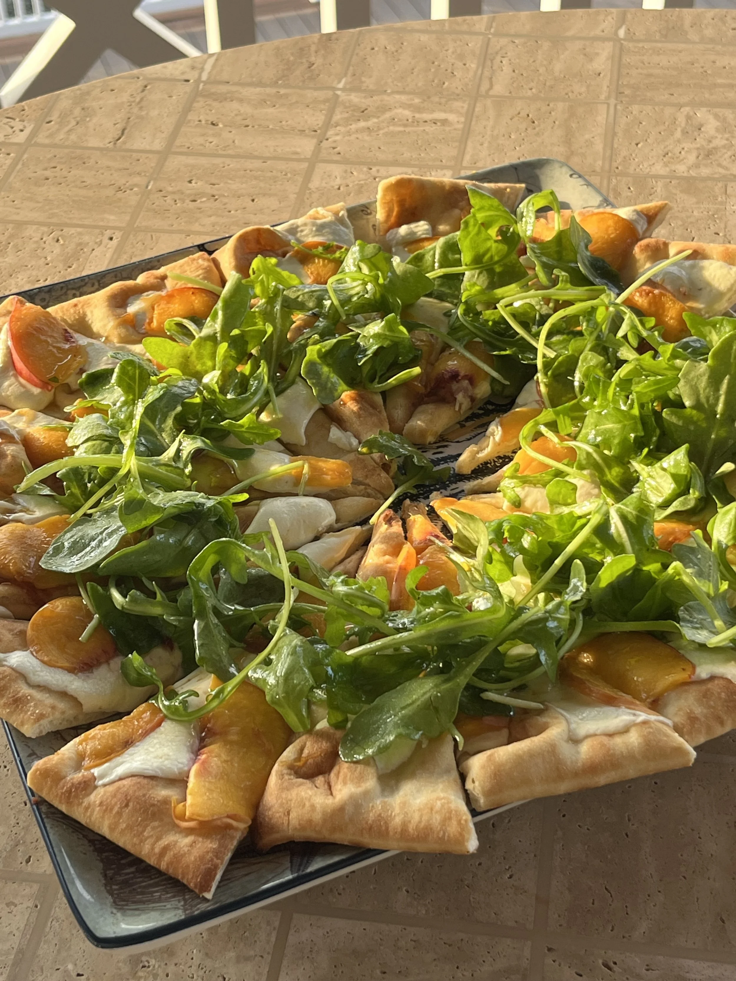 A flatbread with slices of grilled peach and mozzarella topped with baby arugula salad.