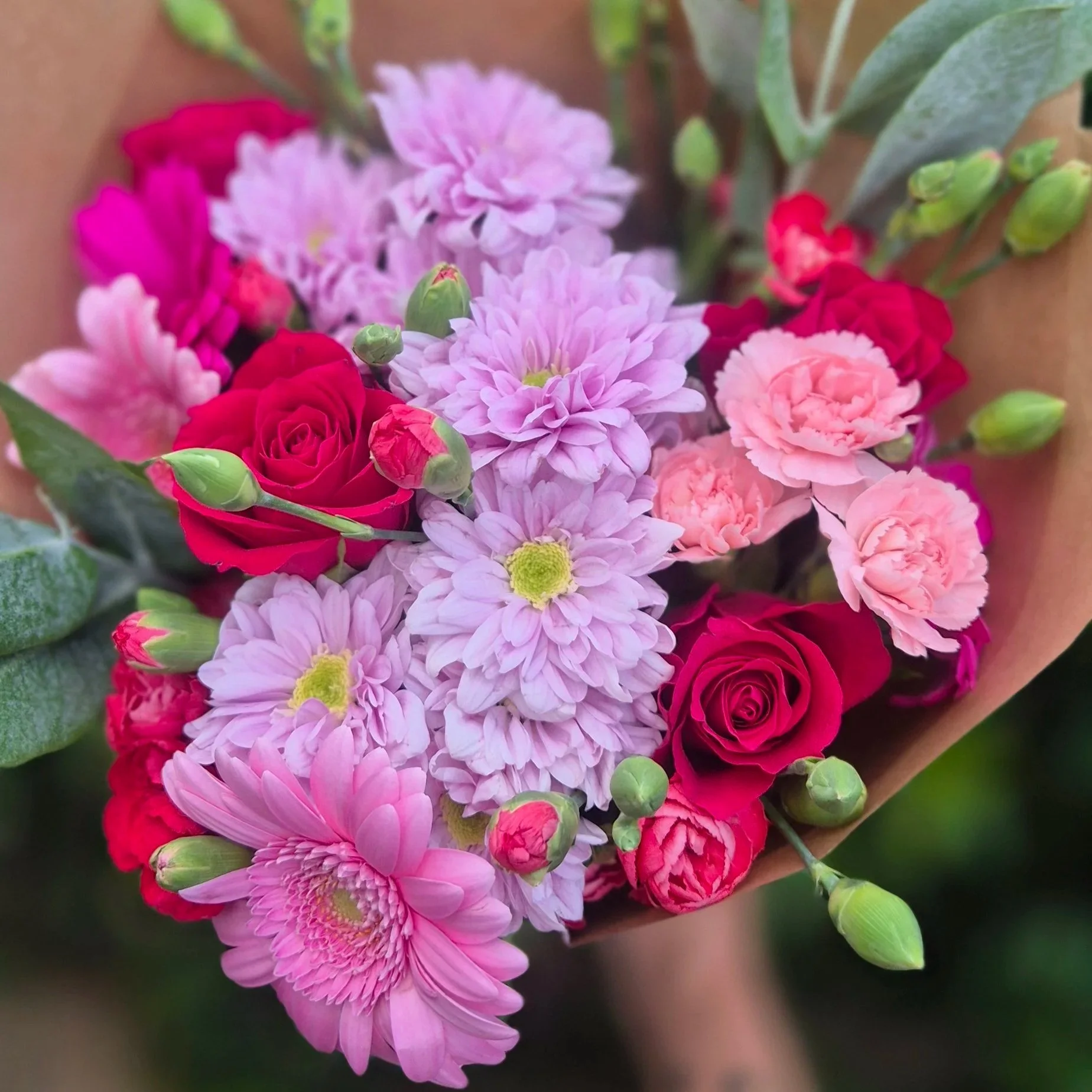 Close-up of a mixed bouquet of pink, purple, and red flowers with green buds and leaves.
