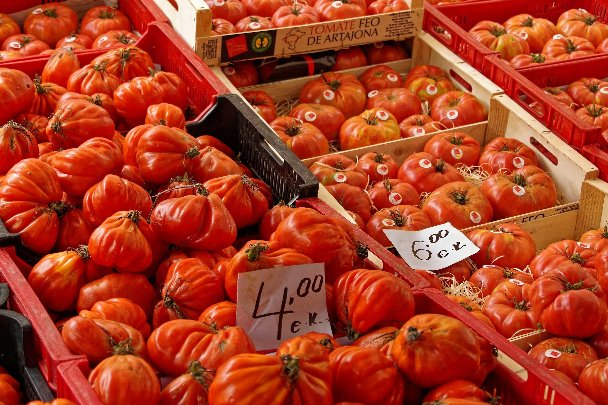 Multiple crates filled with large, ripened heirloom tomatoes at a grocery store or market, with price signs visible.