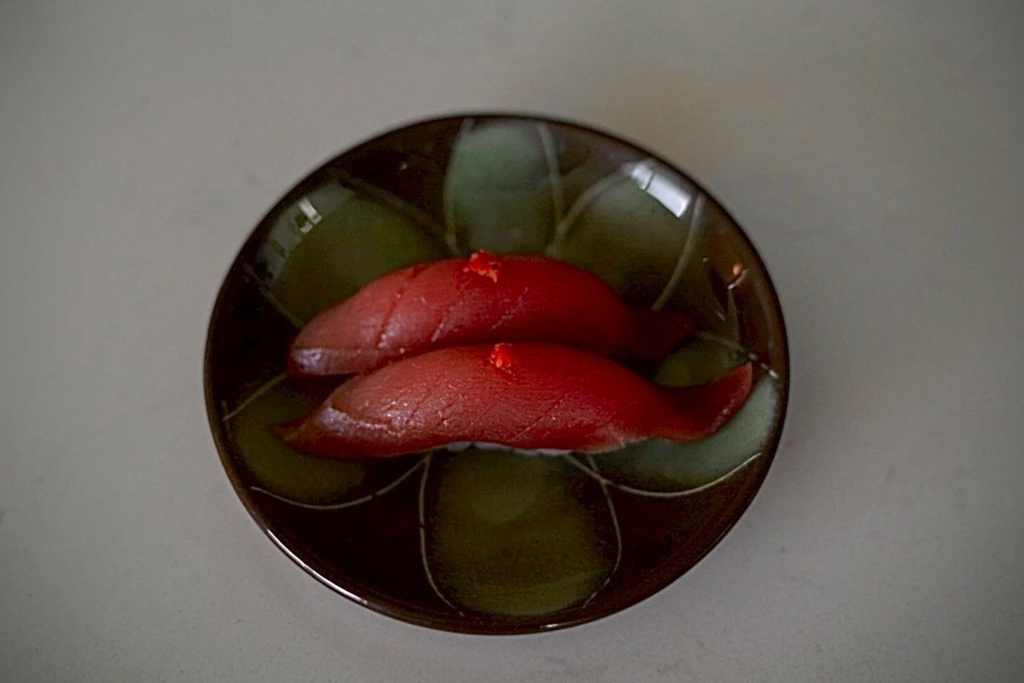 Two pieces of tuna nigiri on a dark brown colored plate