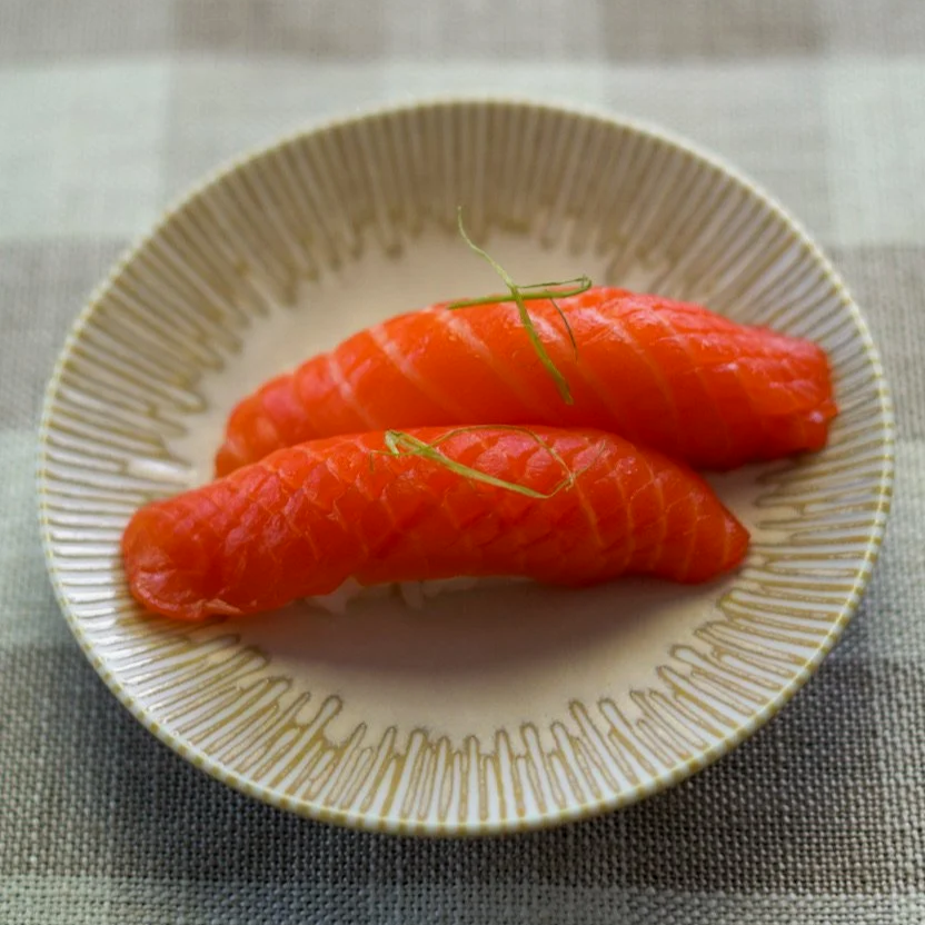 Two pieces of salmon nigiri topped with thinly sliced green onion on a light cream colored plate