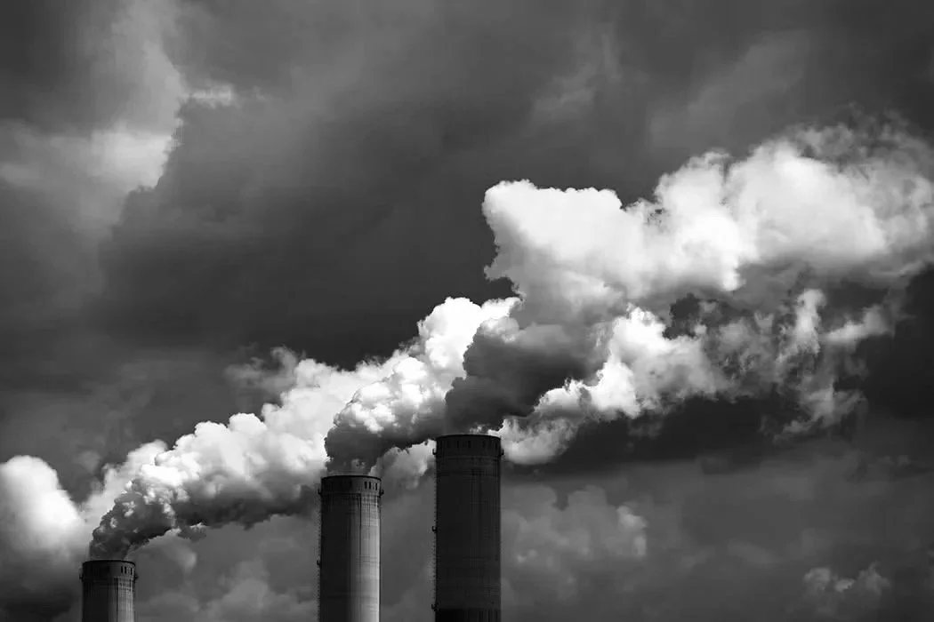 Three smokestacks releasing smoke into a dark cloudy sky.