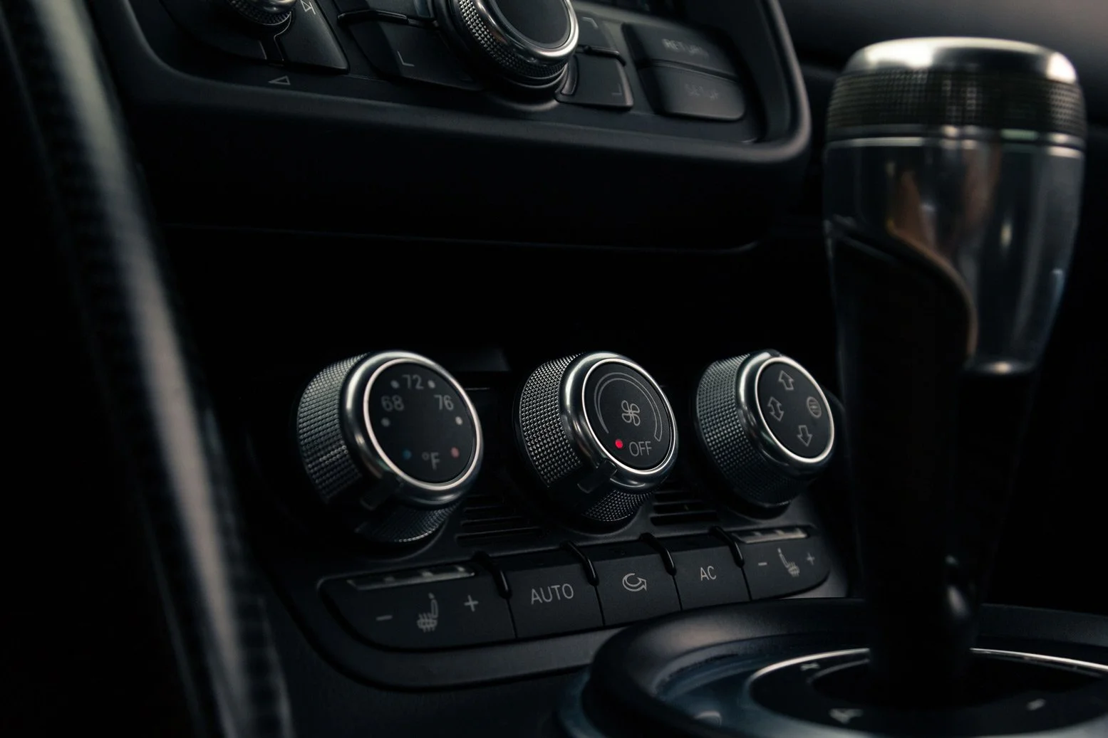 Close-up of Audi R8 GT climate control dials, including temperature, fan speed, and air circulation settings, with a dark background and shifter in the car.