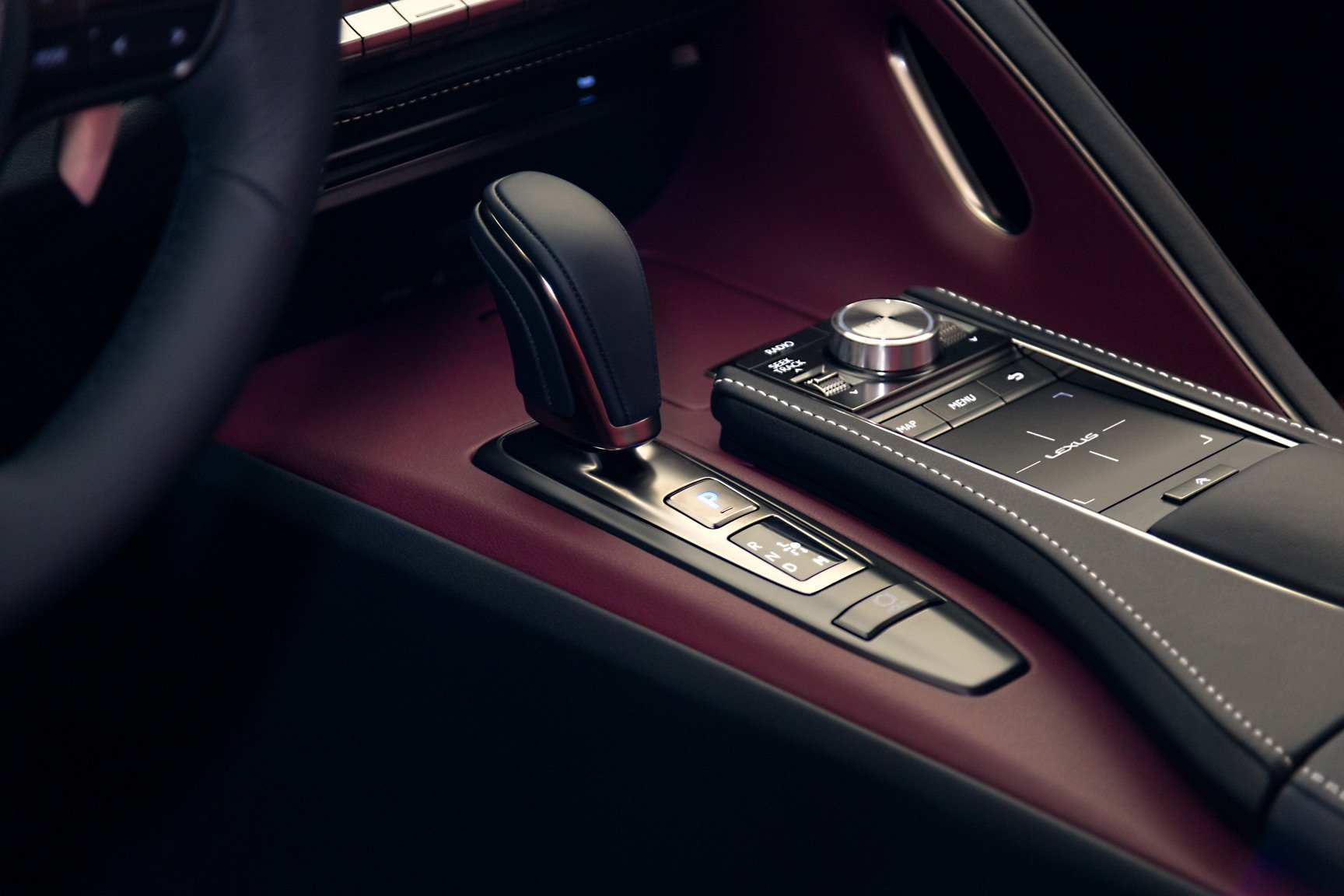 Close-up of the gear shift and control panel in a Lexus car interior, with a black and burgundy color scheme and leather accents.