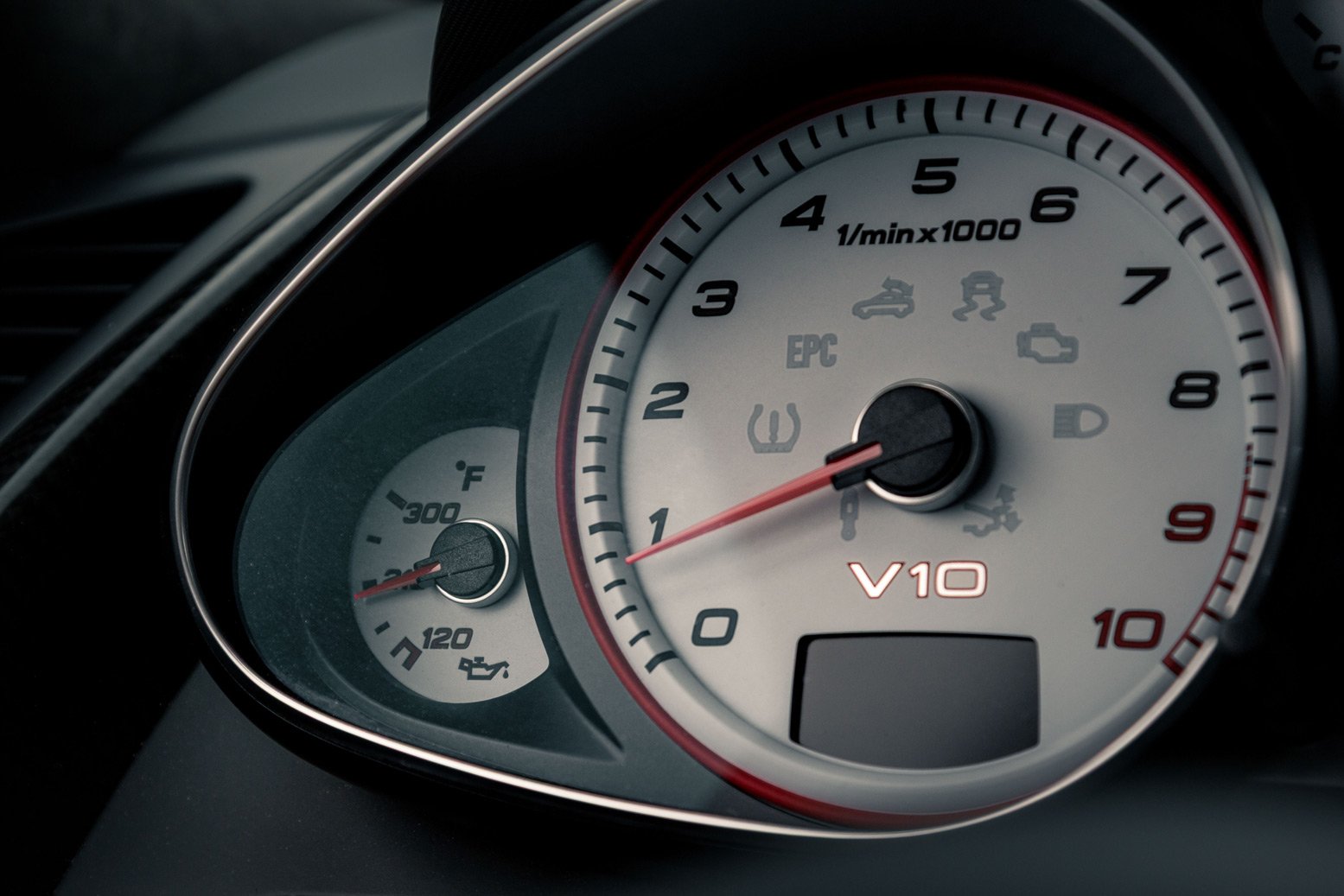 Close-up of an Audi R8 GT dashboard with a tachometer showing approximately 1,100 RPM, a small temperature gauge, and warning lights including tire pressure, EPC, traction control, check engine, and other indicators.