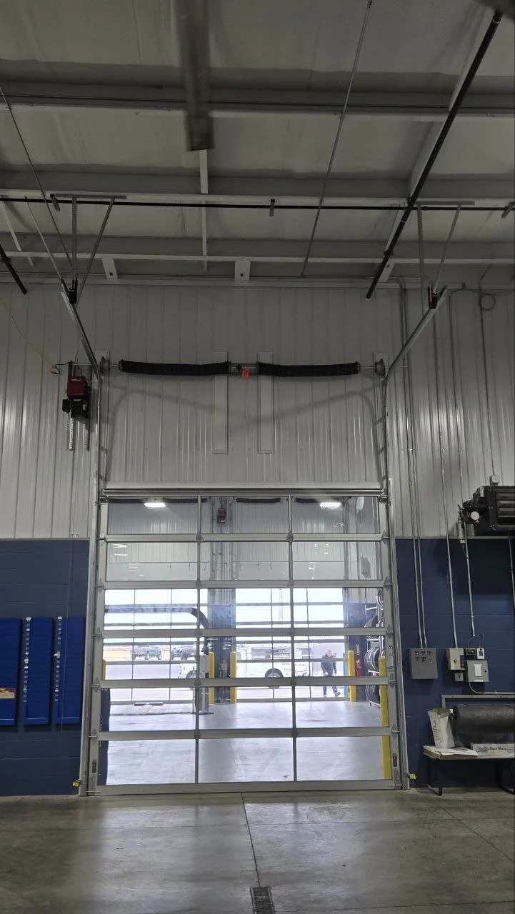 View of a commercial garage door inside an industrial warehouse with the exterior visible through the glass panels.