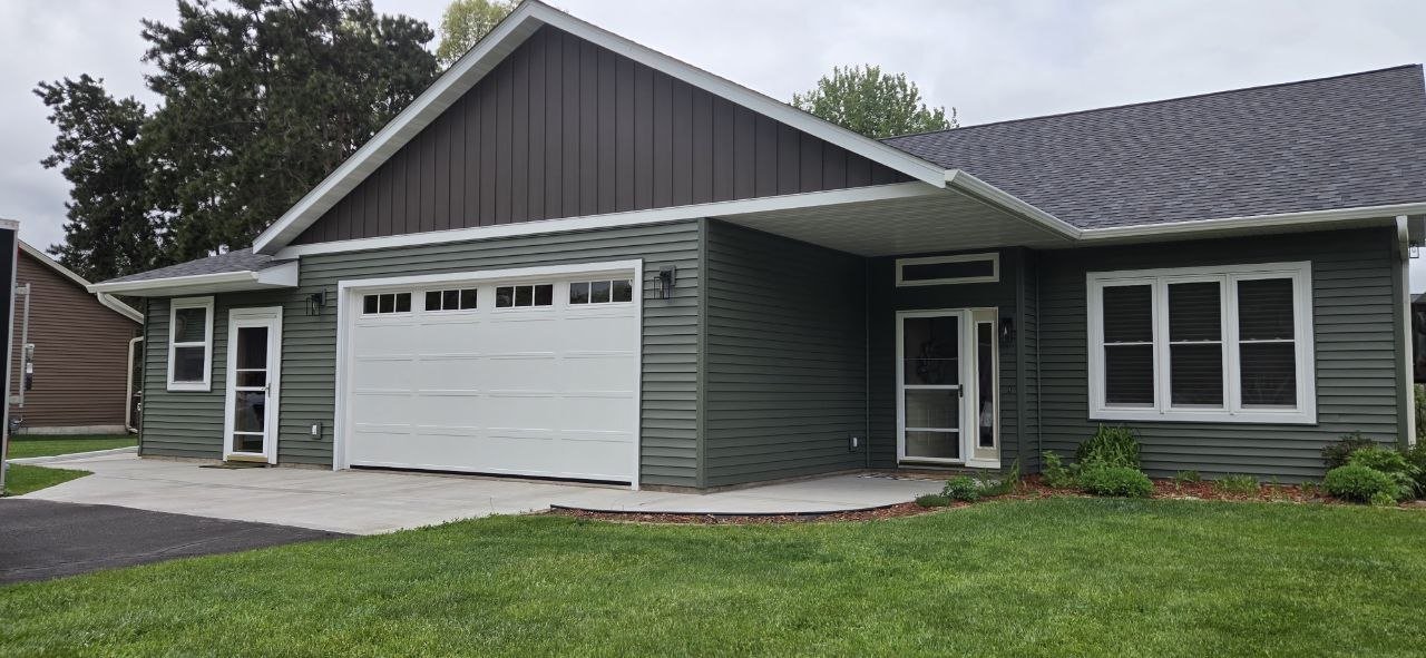 Front view of a green house with white garage door and windows, a small front porch, and a well-maintained lawn.