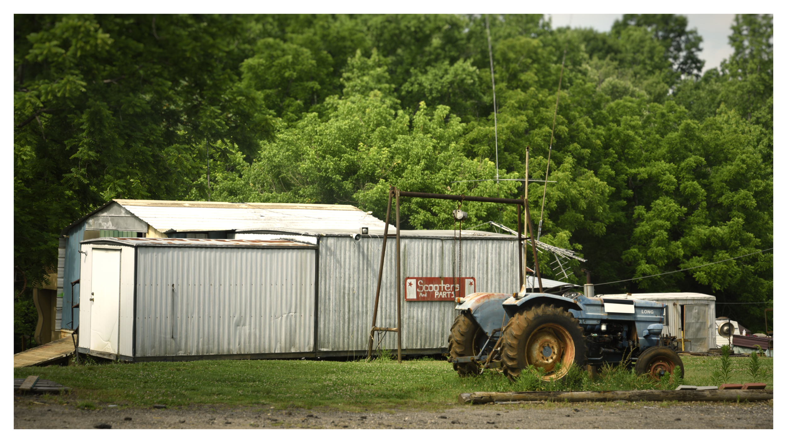 A farm scene with an old blue tractor and a metal shed, with lush green trees in the background