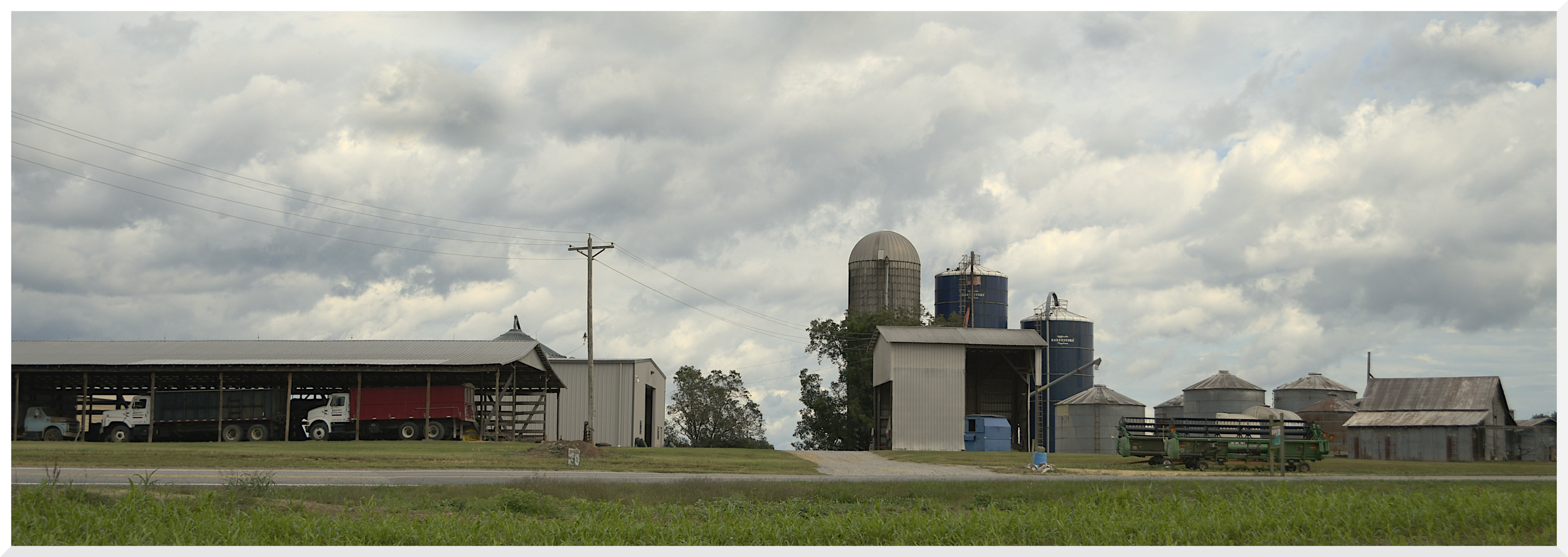 Farm with silos, barns, trucks, and green fields under cloudy sky.