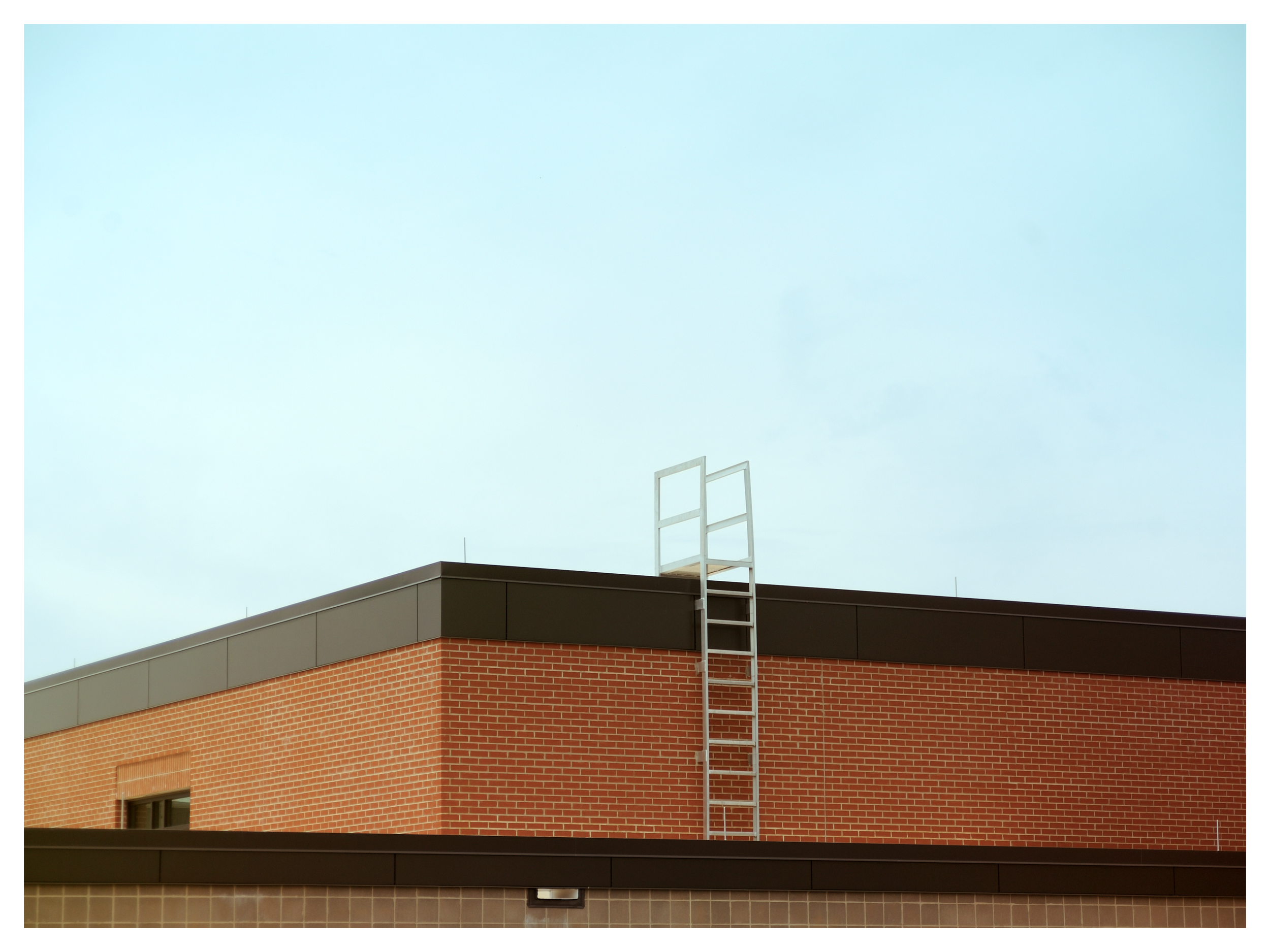 The roof of a brick building with a black overhang and a window, against a clear sky with a ladder and a metal structure on the roof.