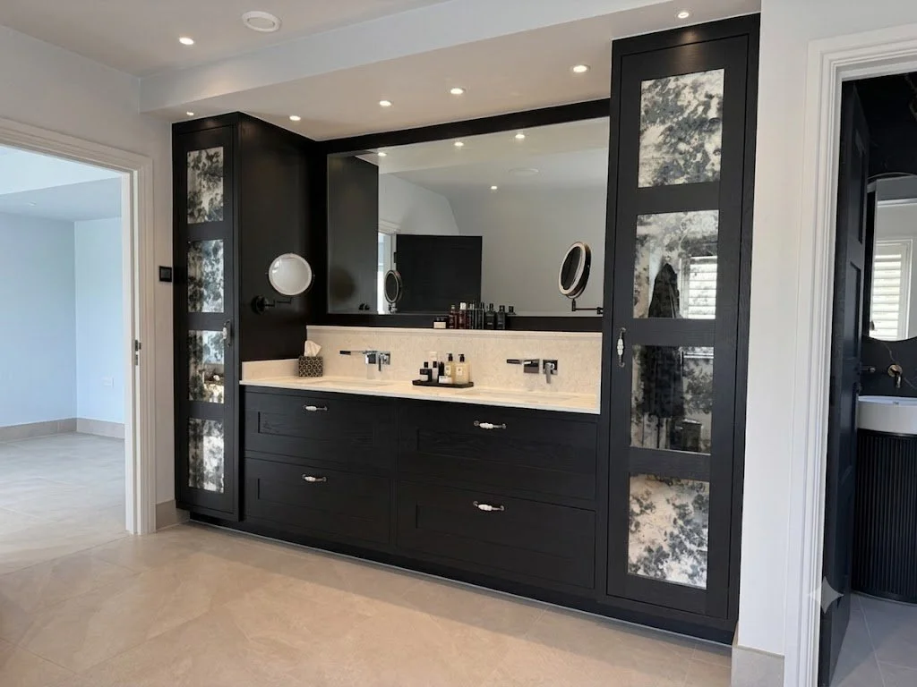 Bespoke modern double vanity unit with ebonized black wood cabinets, quartz countertops, and flanking tall cabinets featuring mercury glass panels, in Hertfordshire by Ken Pope Custom Joinery.