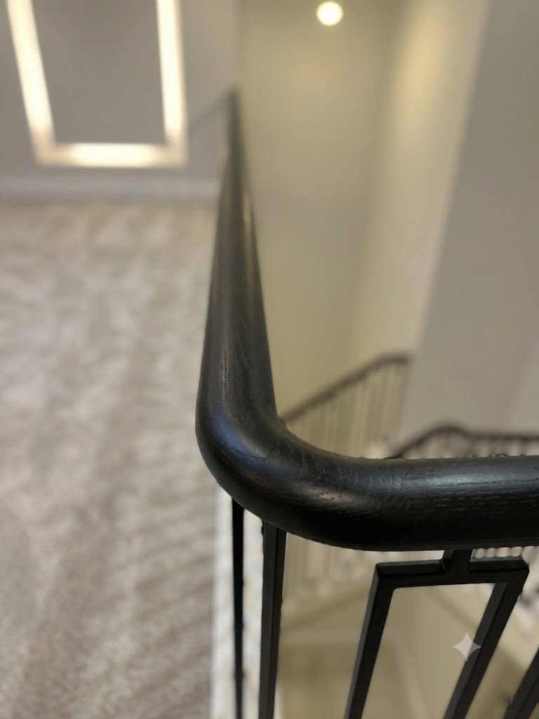 Close-up detail of a continuous ebonized black oak wreathed handrail showing grain texture and smooth curved joint transition by Ken Pope Custom Joinery in Welwyn Hertfordshire
