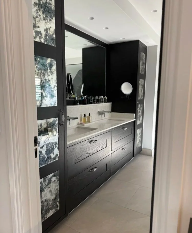 Bespoke ebonized black oak double vanity unit with quartz worktop, wall-mounted taps, and antiqued mirror tall storage cabinets in Welwyn Hertfordshire by Ken Pope Custom Joinery