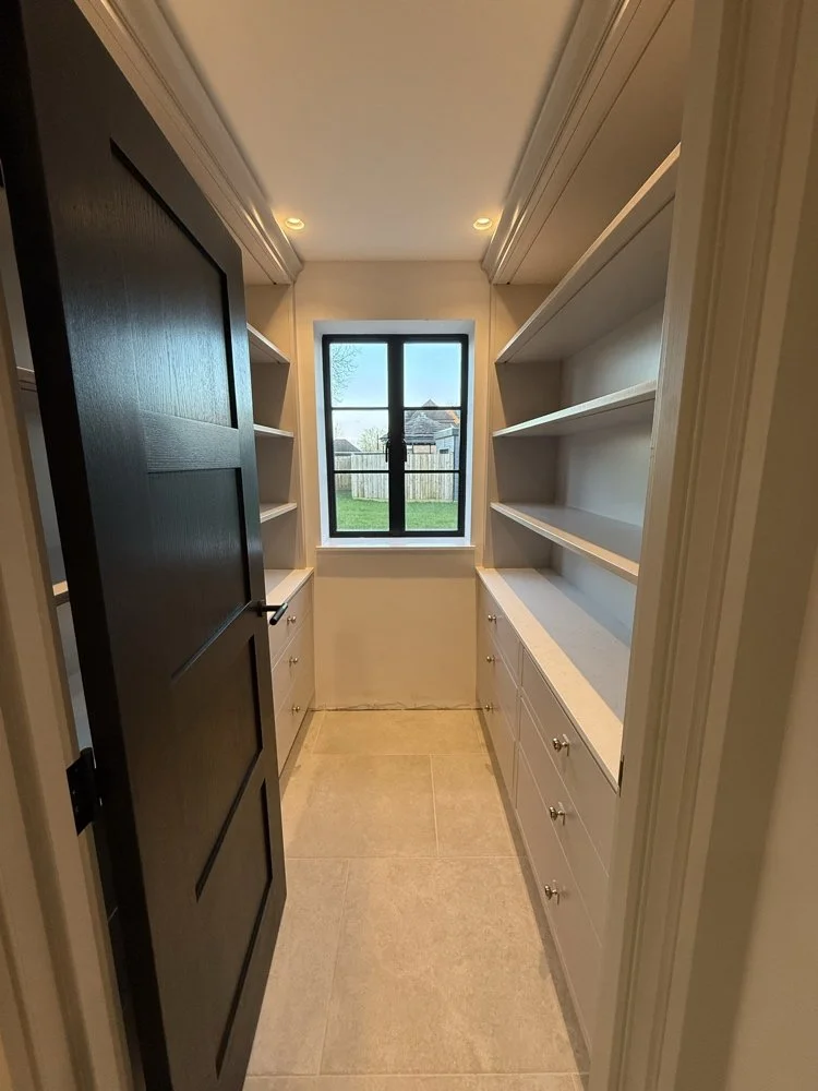 Walk-in pantry suite viewed through an ebonized black oak door featuring painted in-frame cabinetry, quartz worktops, and open display shelving in Welwyn Hertfordshire by Ken Pope Custom Joinery