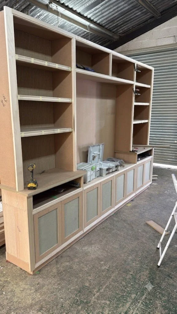 Large custom media wall unit with reeded back panels undergoing dry-fit assembly on the workshop floor