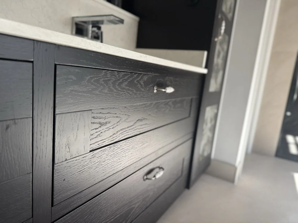 Close-up detail of ebonized black oak vanity drawer fronts showing deep wood grain texture, quartz worktop, and polished handles in Welwyn Hertfordshire by Ken Pope Custom Joinery