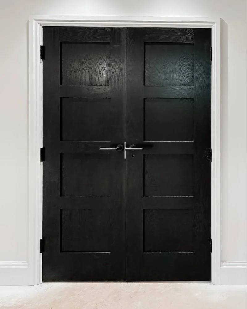 Symmetrical four-panel ebonized black oak double doors with modern black lever handles set in white architraves in Welwyn Hertfordshire by Ken Pope Custom Joinery