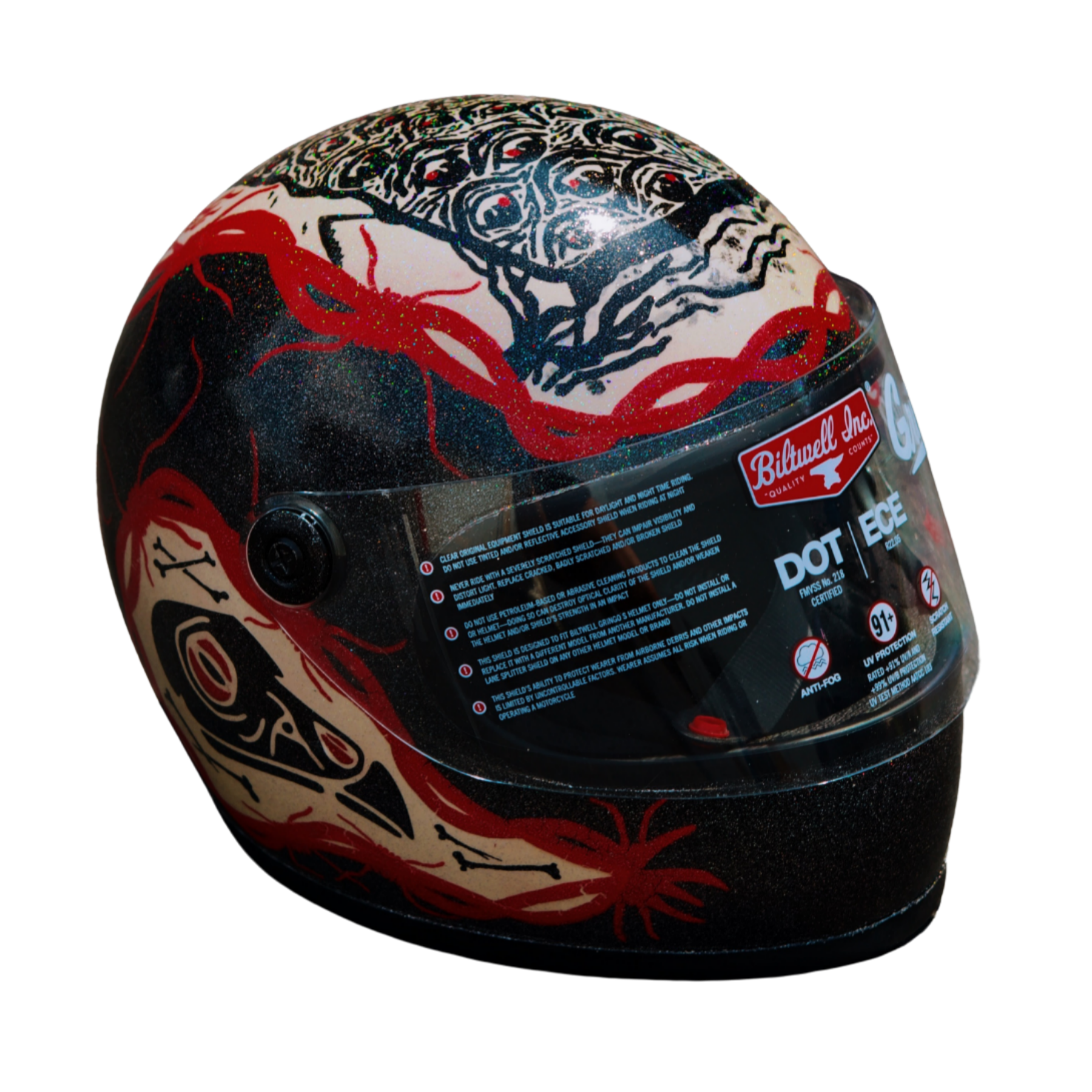 A black full-face motorcycle helmet with red and white intricate design patterns, including a spider graphic, and a clear visor with warning labels and brand logo.