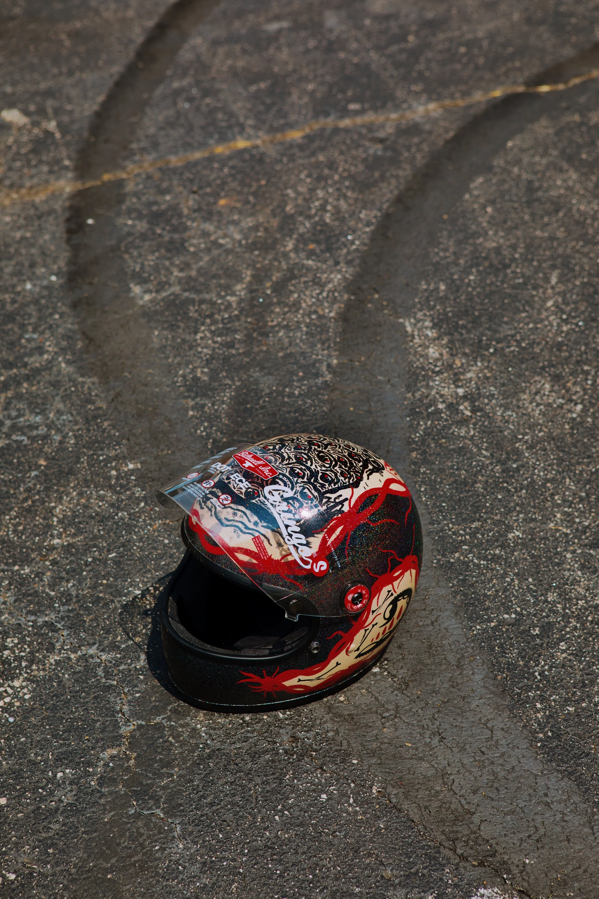 A motorcycle helmet with a black base and red flame design on a cracked asphalt surface.