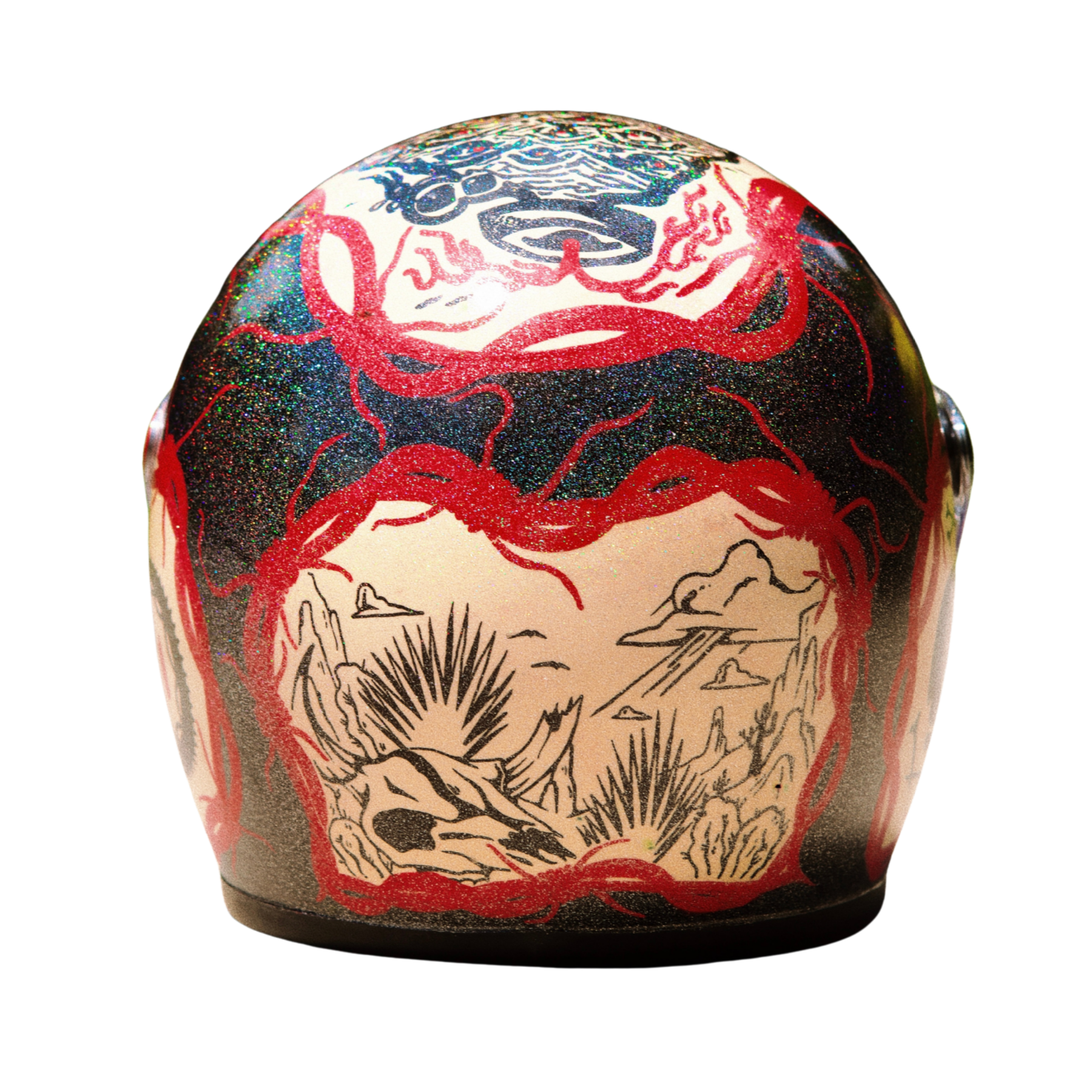 Close-up of a decorative object, possibly a stone or ceramic, with detailed tattoo-style artwork. The artwork includes red, black, and glittery blue patterns, depicting a skull, mountains, and sun rays.