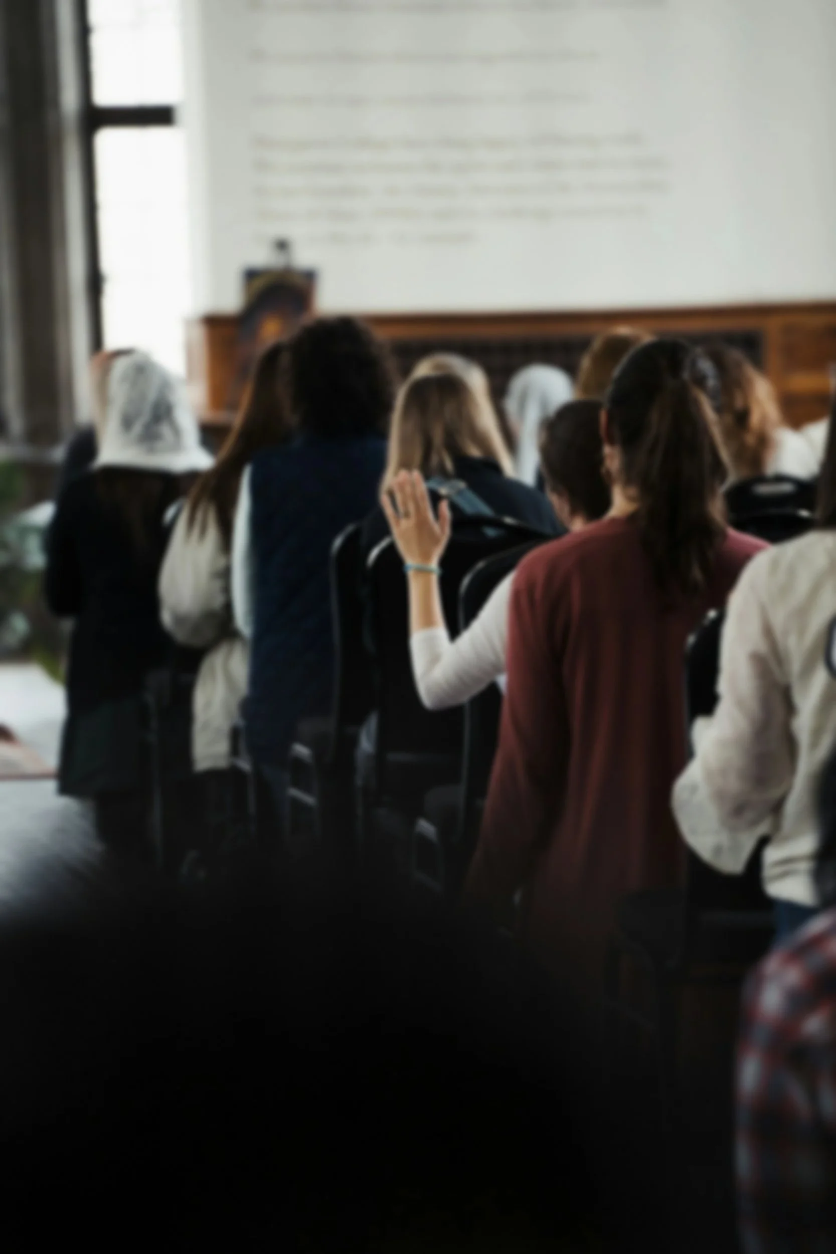 A group of people sitting in a classroom or lecture hall, facing a large screen or board at the front of the room.