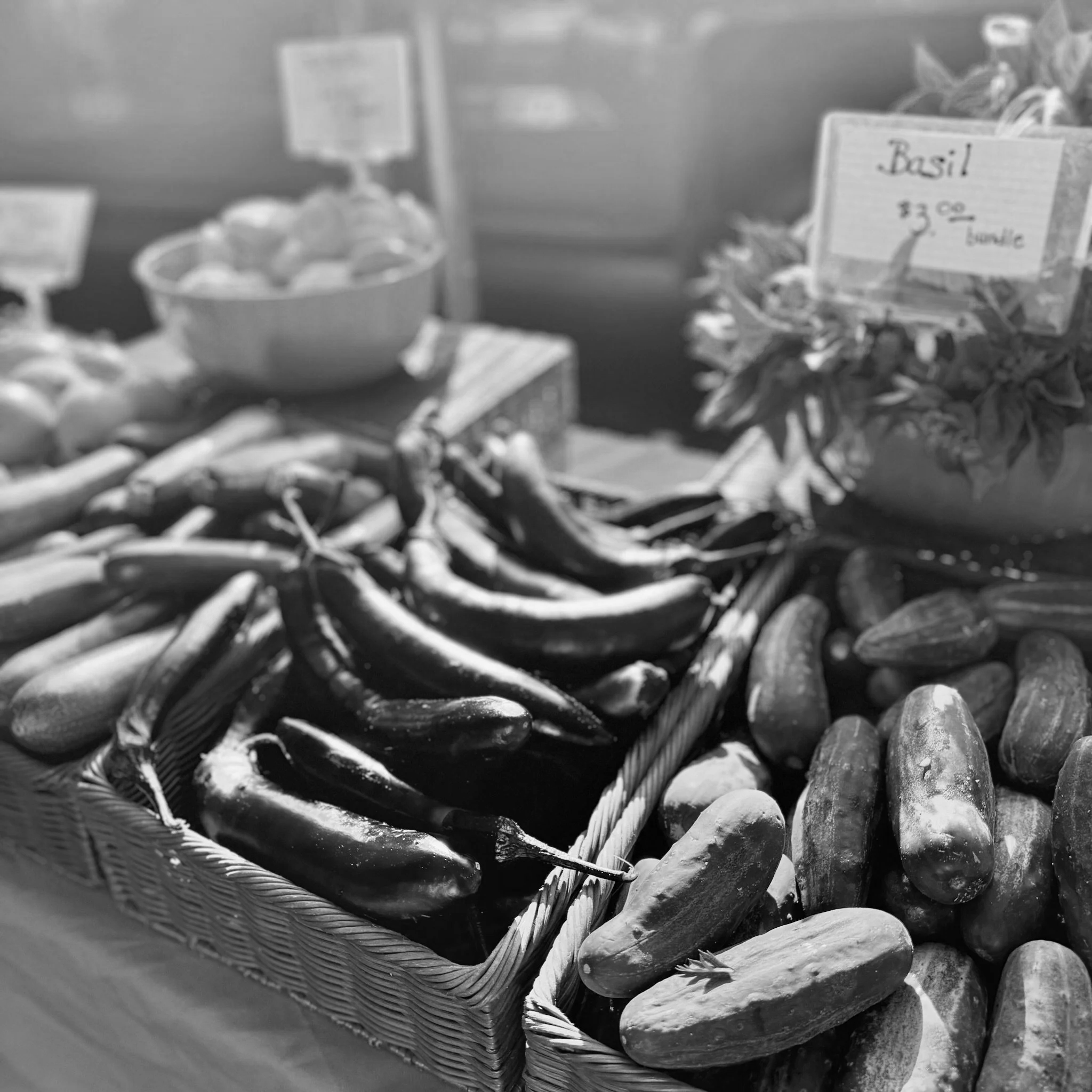 Close-up of a woven basket filled with garlic bulbs, with a handwritten sign that reads 'Basil 3.00', on a market stall.