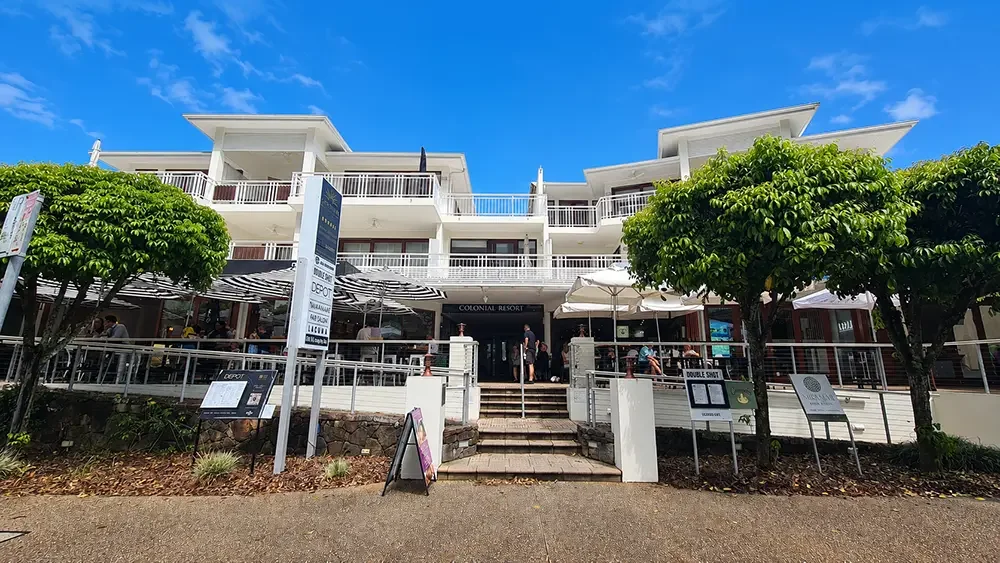 A modern multi-story strata building at the Sunshine Coast, with outdoor seating, trees, and a clear blue sky, in a contemporary colour scheme.