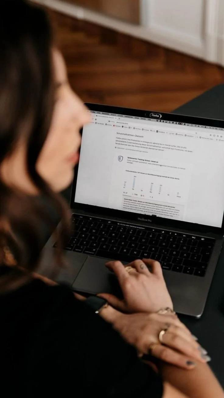 Une femme regarde un ordinateur portable affichant un document ou une page web. La mise au point est floue sur la femme, tandis que l'écran de l'ordinateur est plus clair.