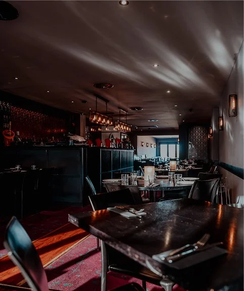 Interior of an upscale restaurant with dark wood tables, chairs, and dim lighting.