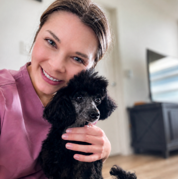 Kaitlyn, owner of The Gentle Shepherd Anesthesia-Free Canine Dental Cleaning, holding a client's black poodle puppy.