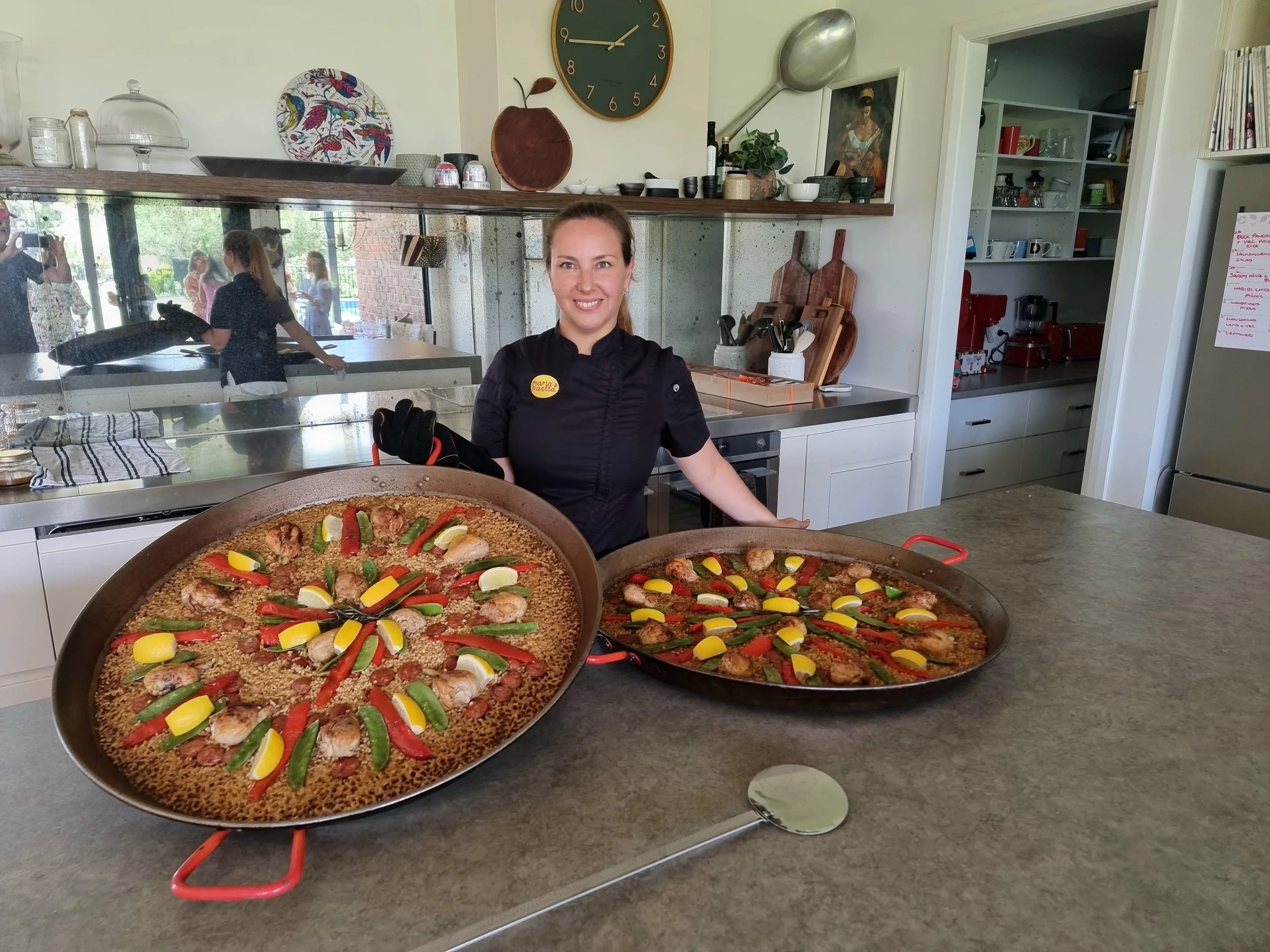 Maria Vicencio Munchmeyer paella specialist holding two pans of paella in kitchen