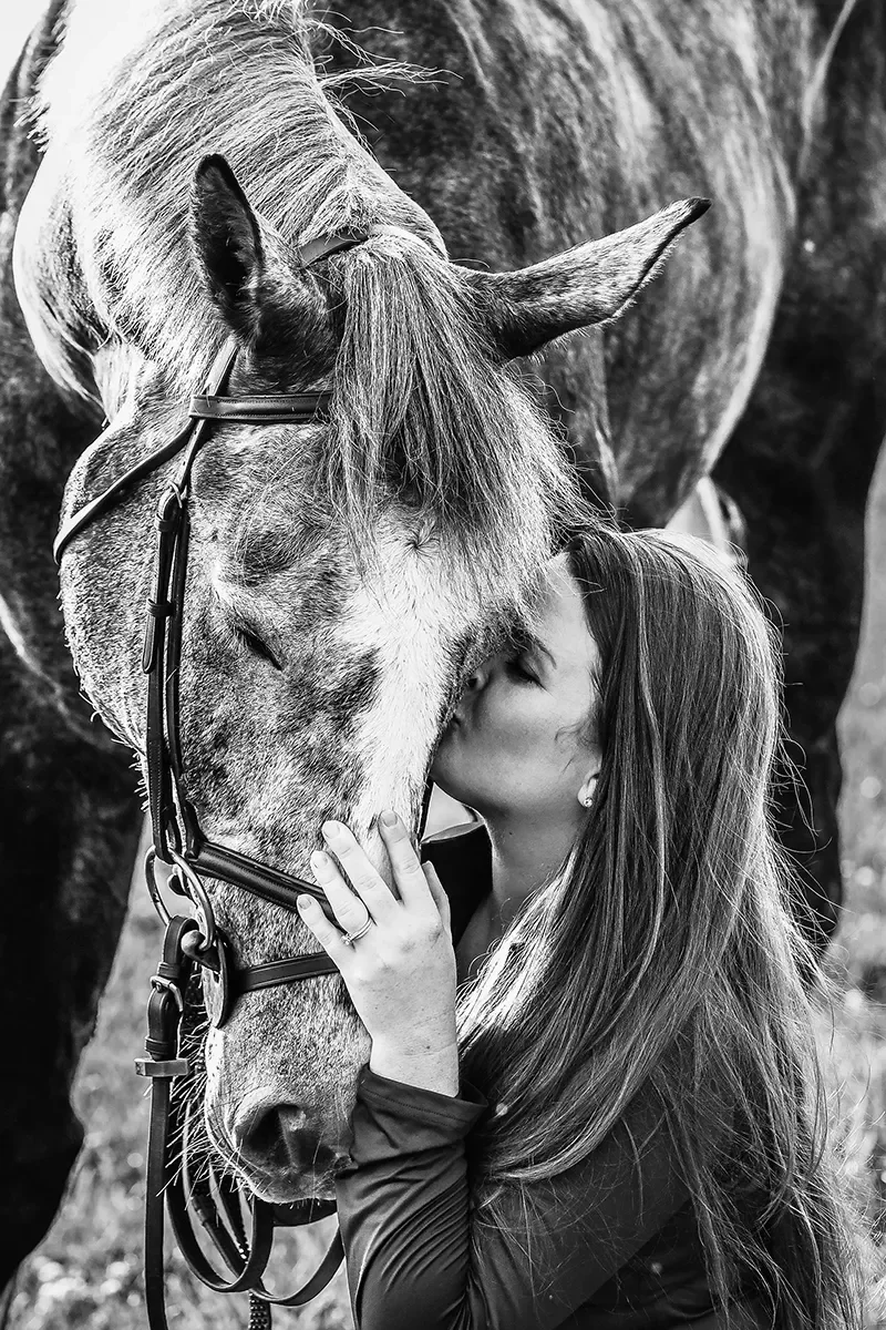 A woman kissing a horse on the nose, both with eyes closed, in black and white.