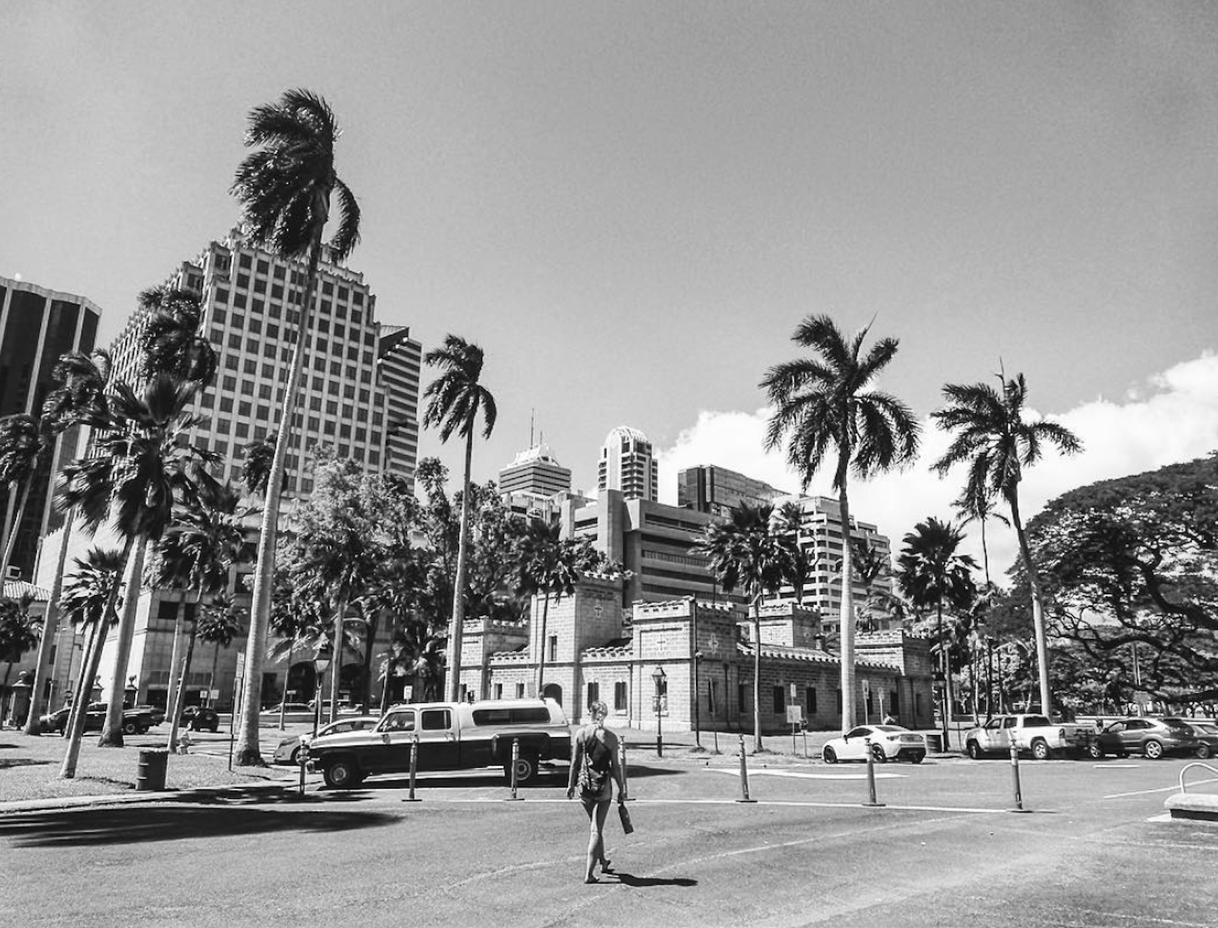 Black and white of Maria walking toward tall buildings and palm trees in Honolulu, Hawaii.
